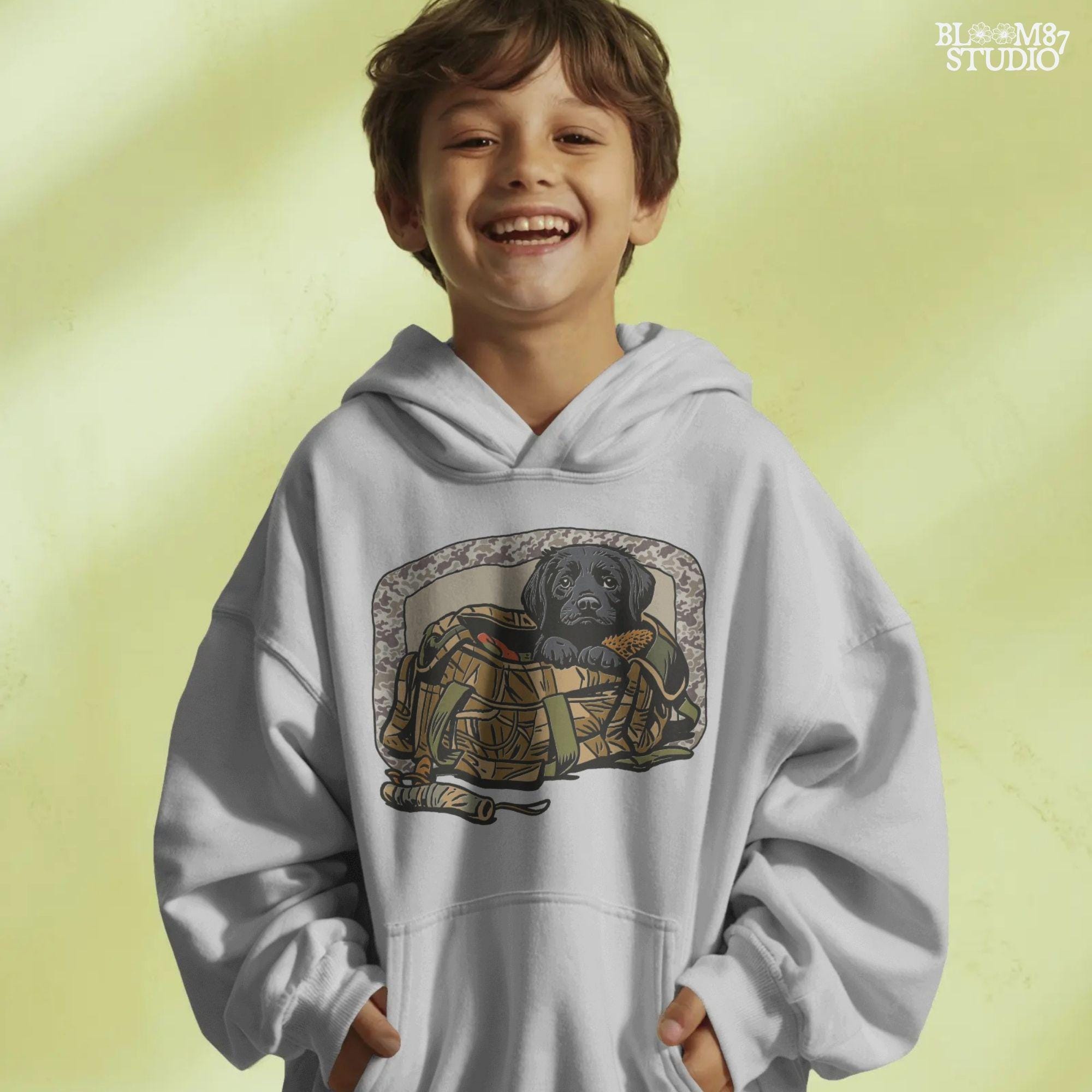 Black Labrador puppy in a camo hunting bag, framed in camouflage pattern, ideal for waterfowl and duck hunting sublimation art.