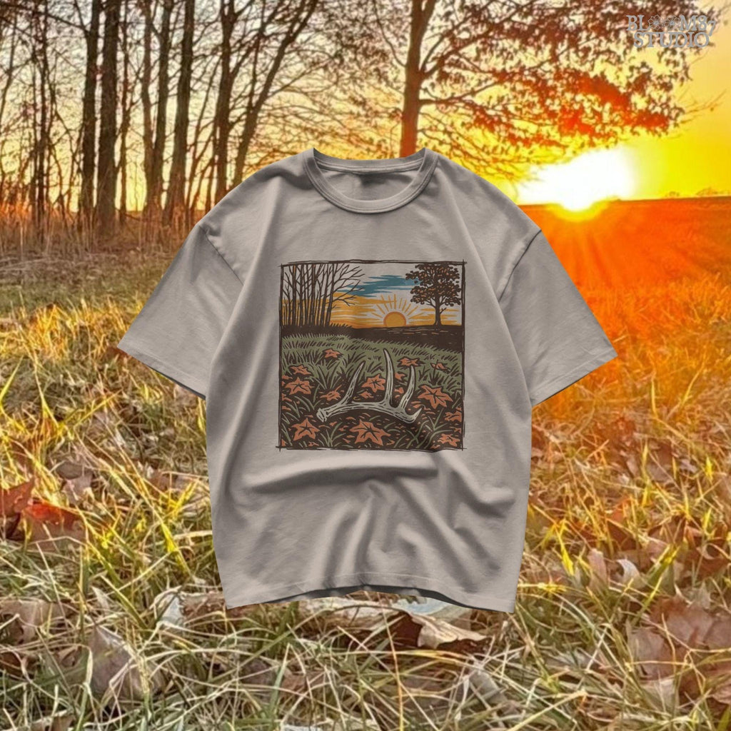 A rustic illustration of a whitetail antler lying in a fall field with orange leaves and a vibrant sunset sky in the background, PNG format for sublimation.
