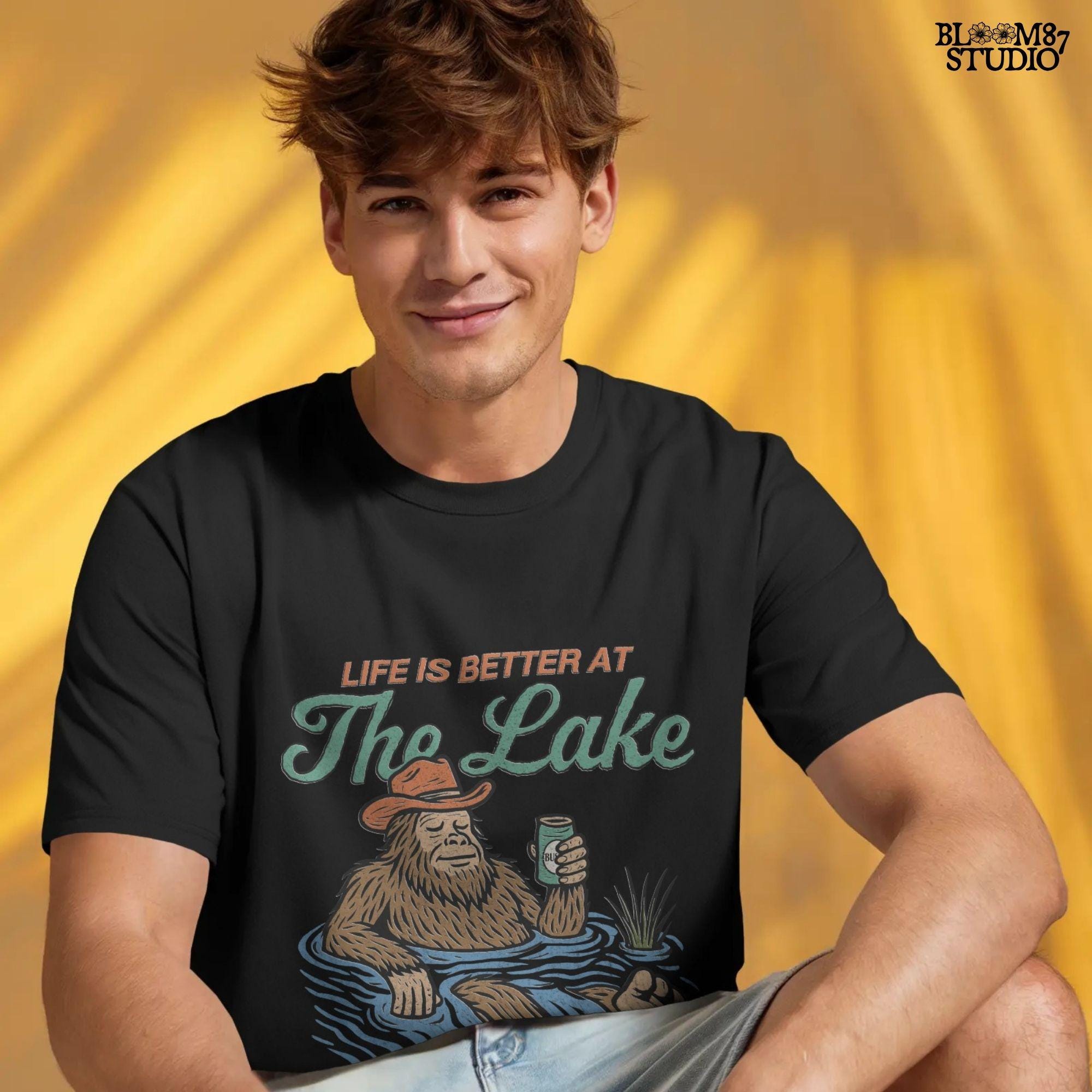 Cartoon Bigfoot relaxing in a lake wearing a cowboy hat, holding a beer can, with retro text saying “Life is Better at the Lake”