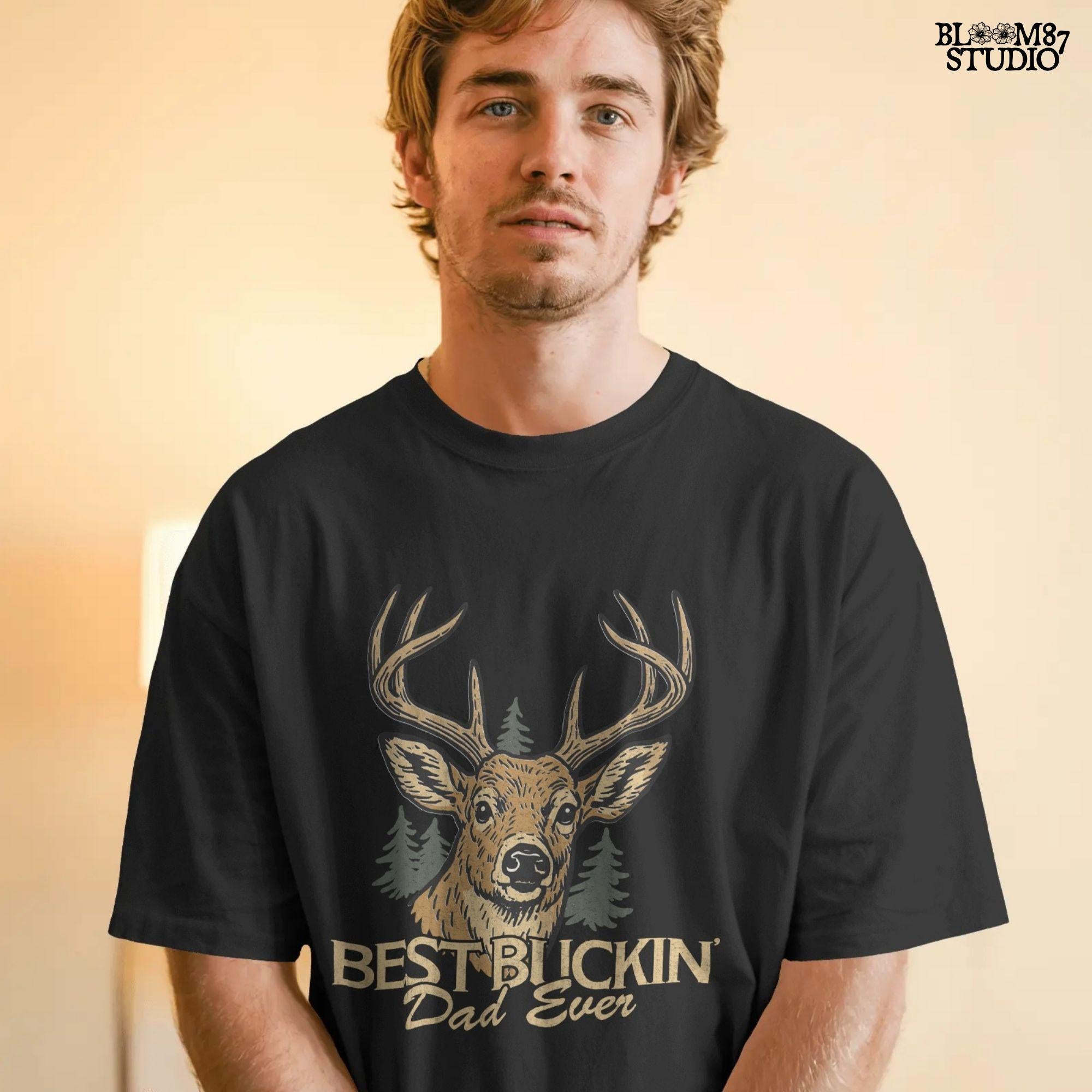 Rustic illustration of a buck deer with antlers and pine trees, text below says “Best Buckin’ Dad Ever” in bold and script font