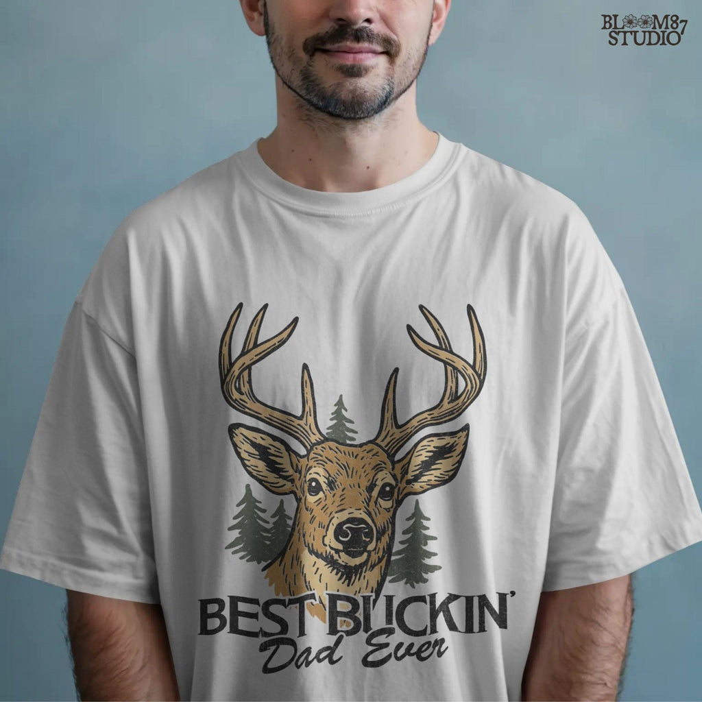 Rustic illustration of a buck deer with antlers and pine trees, text below says “Best Buckin’ Dad Ever” in bold and script font