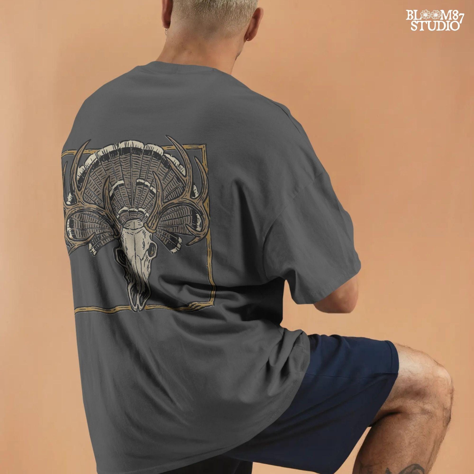 Illustration of a deer skull with antlers set in front of a fanned turkey tail and framed in a rustic square border