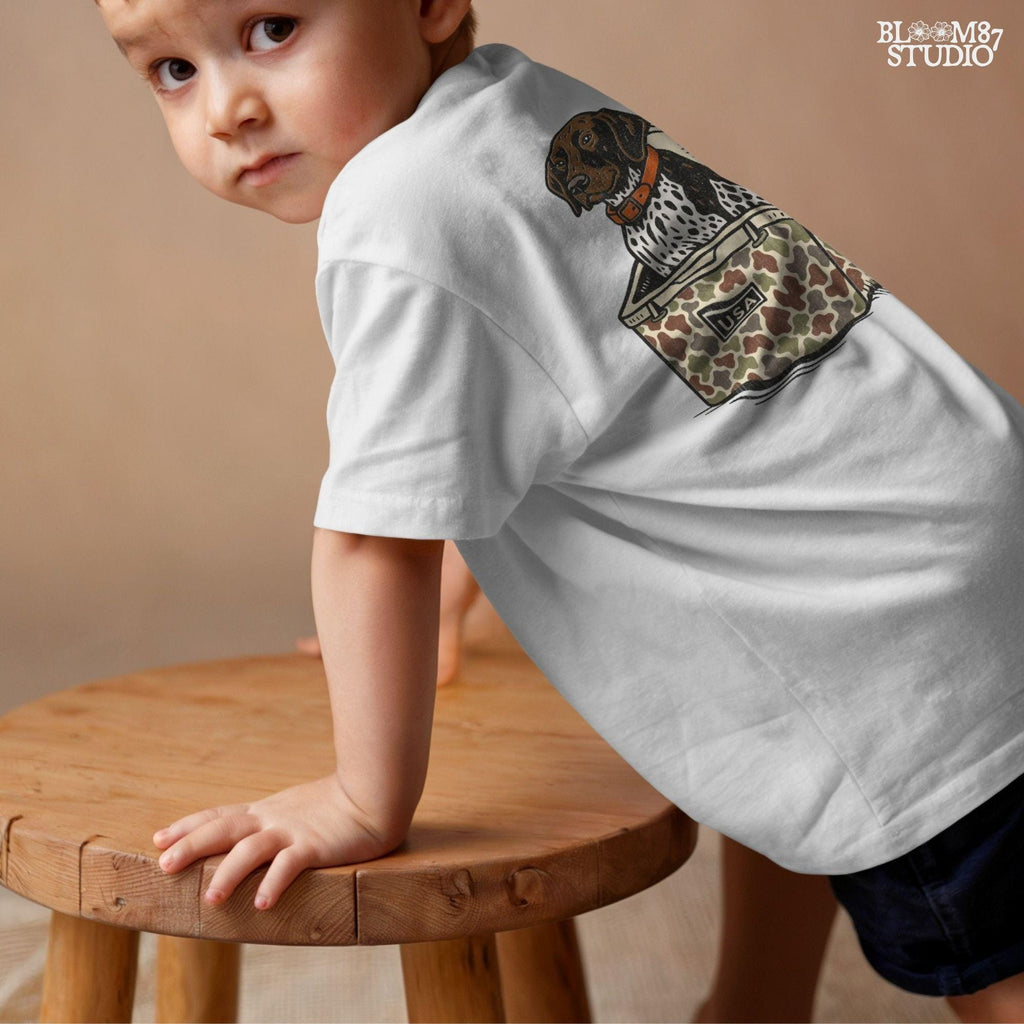 German Shorthaired Pointer dog sitting inside camouflage cooler labeled “USA,” in rustic cartoon patriotic style