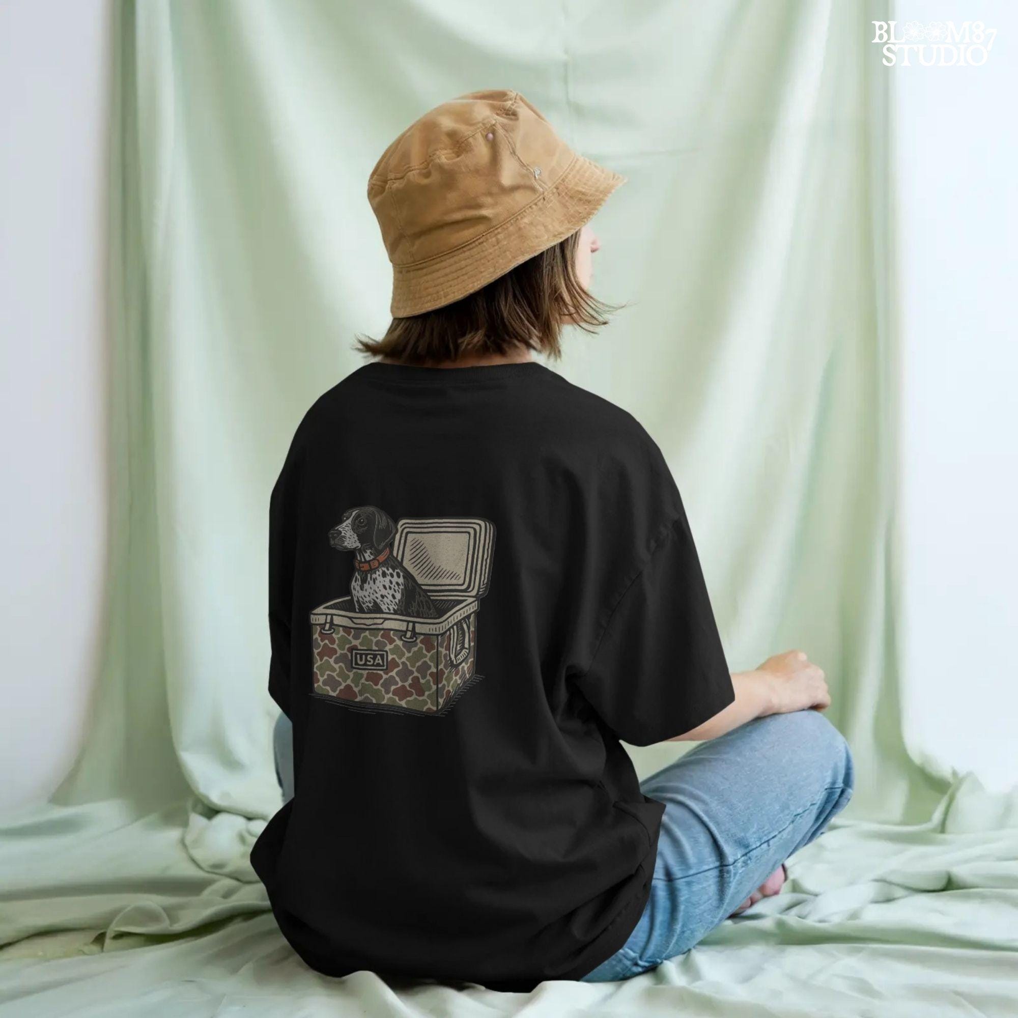 German Shorthaired Pointer dog sitting inside camouflage cooler labeled “USA,” in rustic cartoon patriotic style