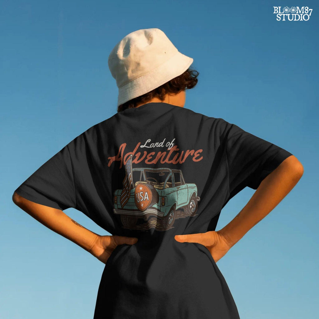 Vintage convertible truck with “USA” spare tire and American flag, text reads “Land of Adventure,” in a retro patriotic illustration style.