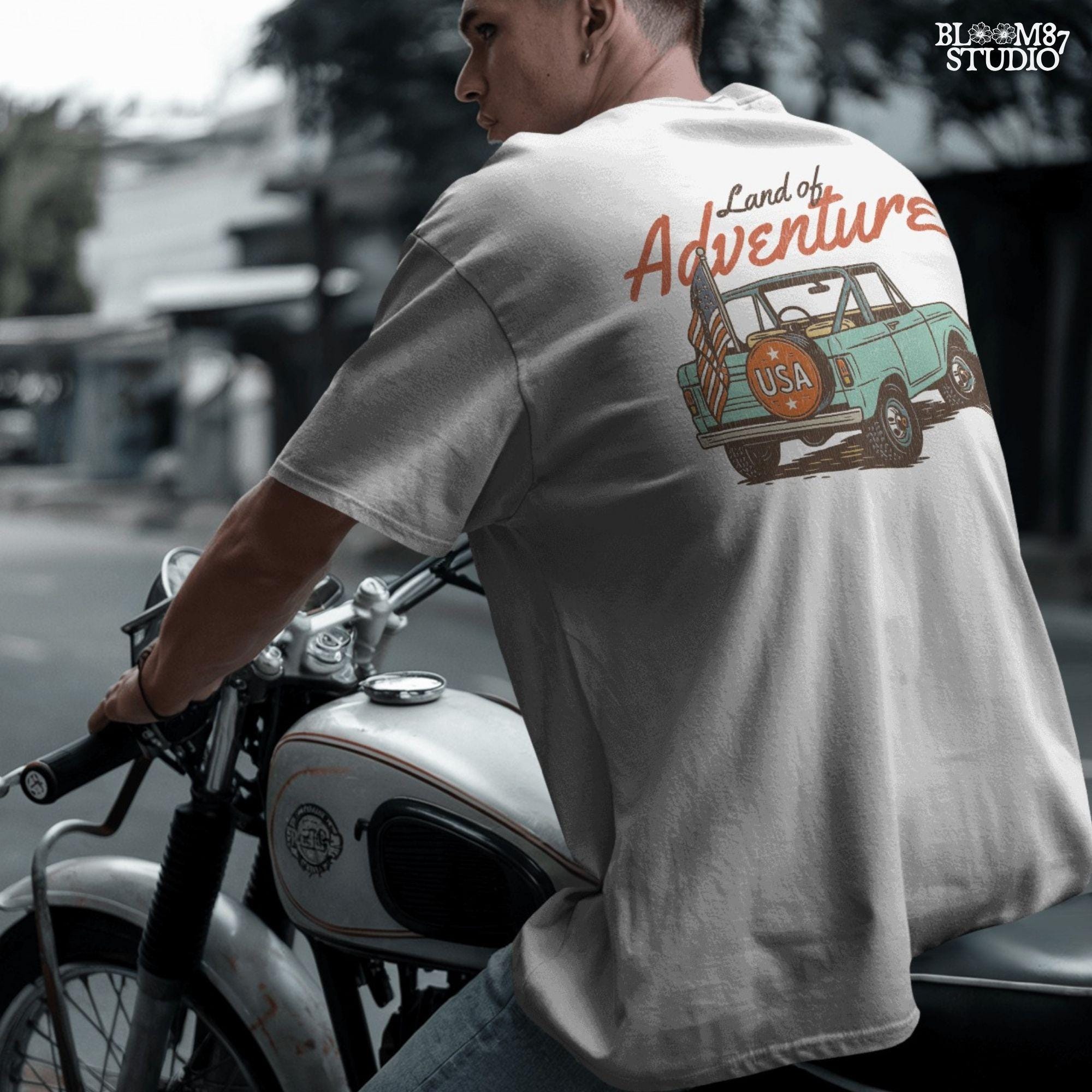 Vintage convertible truck with “USA” spare tire and American flag, text reads “Land of Adventure,” in a retro patriotic illustration style.