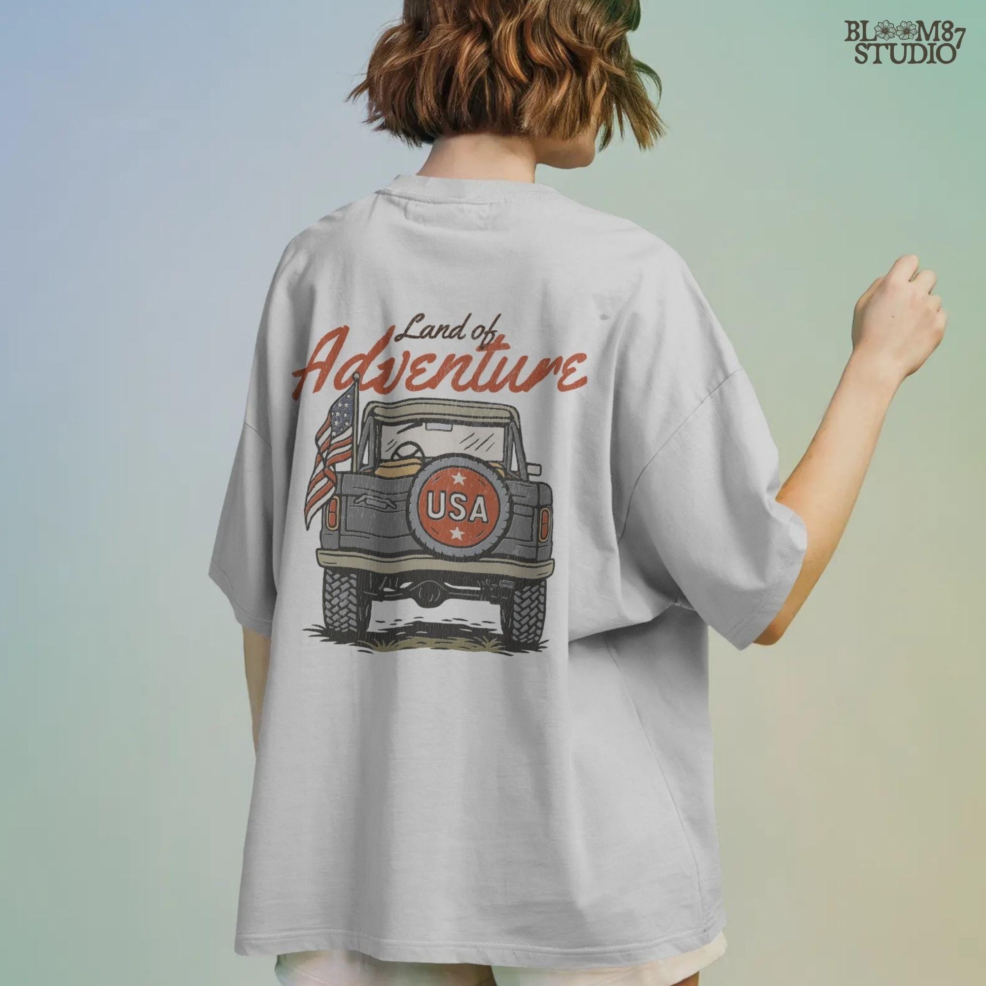 Vintage offroad truck seen from the back with “USA” spare tire and waving American flag, text reads “Land of Adventure” in retro patriotic style.