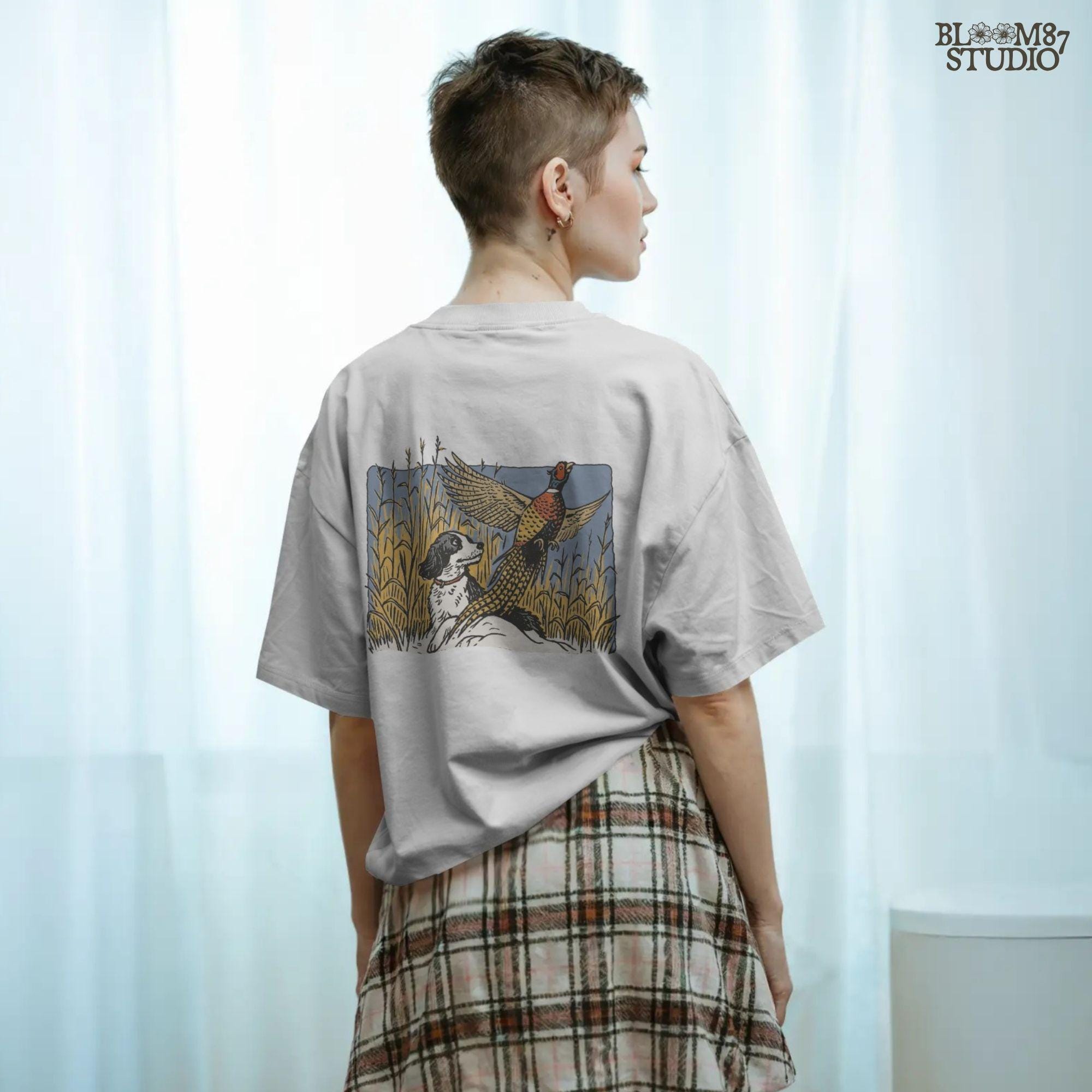 Vintage-style illustration of a black and white hunting dog watching a colorful pheasant take flight in a cornfield, designed for rustic outdoor themes.