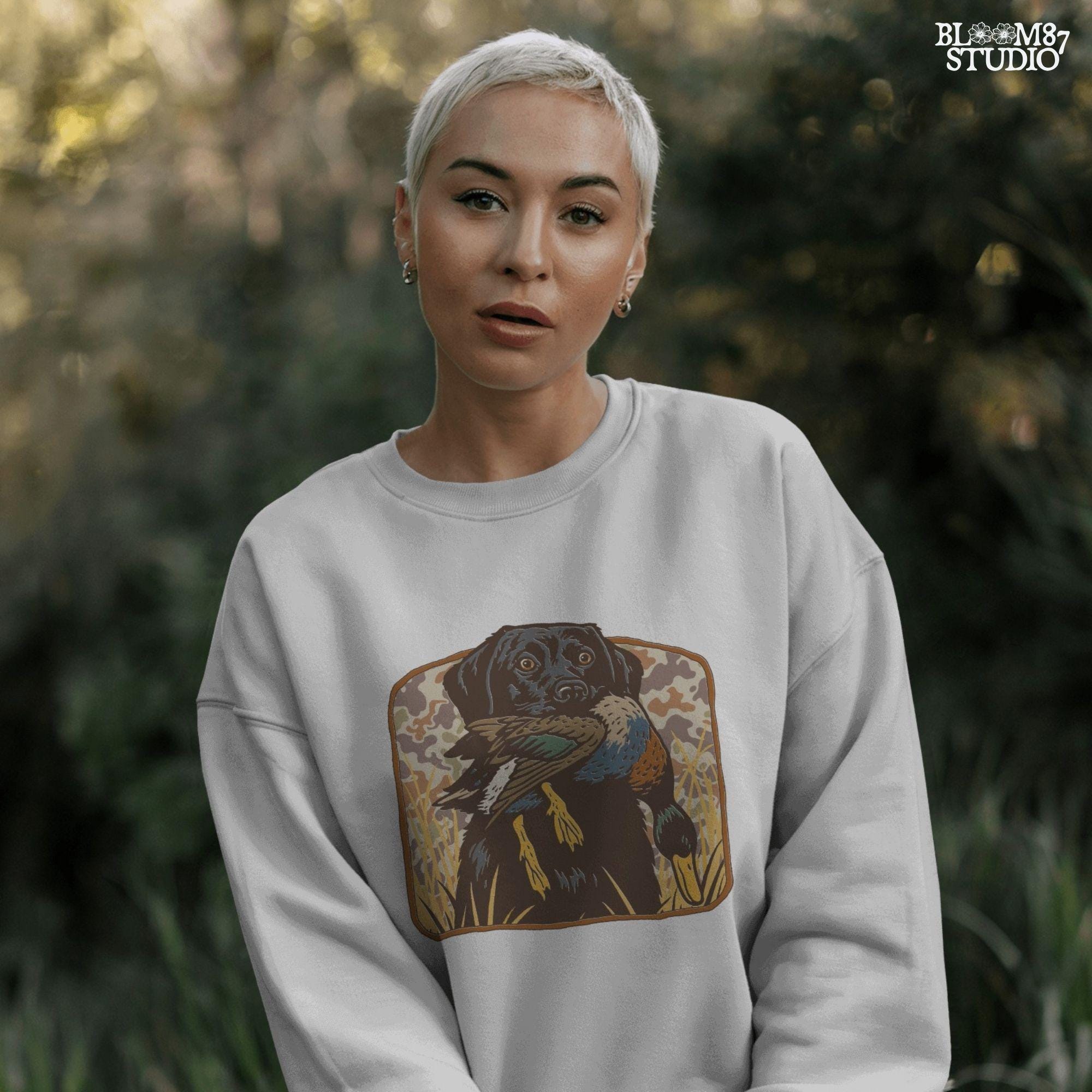 Vintage-style illustration of a black Labrador retriever holding a mallard duck in its mouth with a camouflage background, ideal for duck hunting designs.