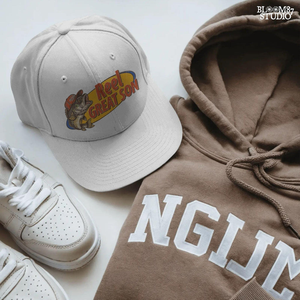 Illustration of a bass fish wearing a red trucker hat with the text “Reel Great Son” in bold vintage lettering, designed for sublimation and fishing-themed gifts for kids.