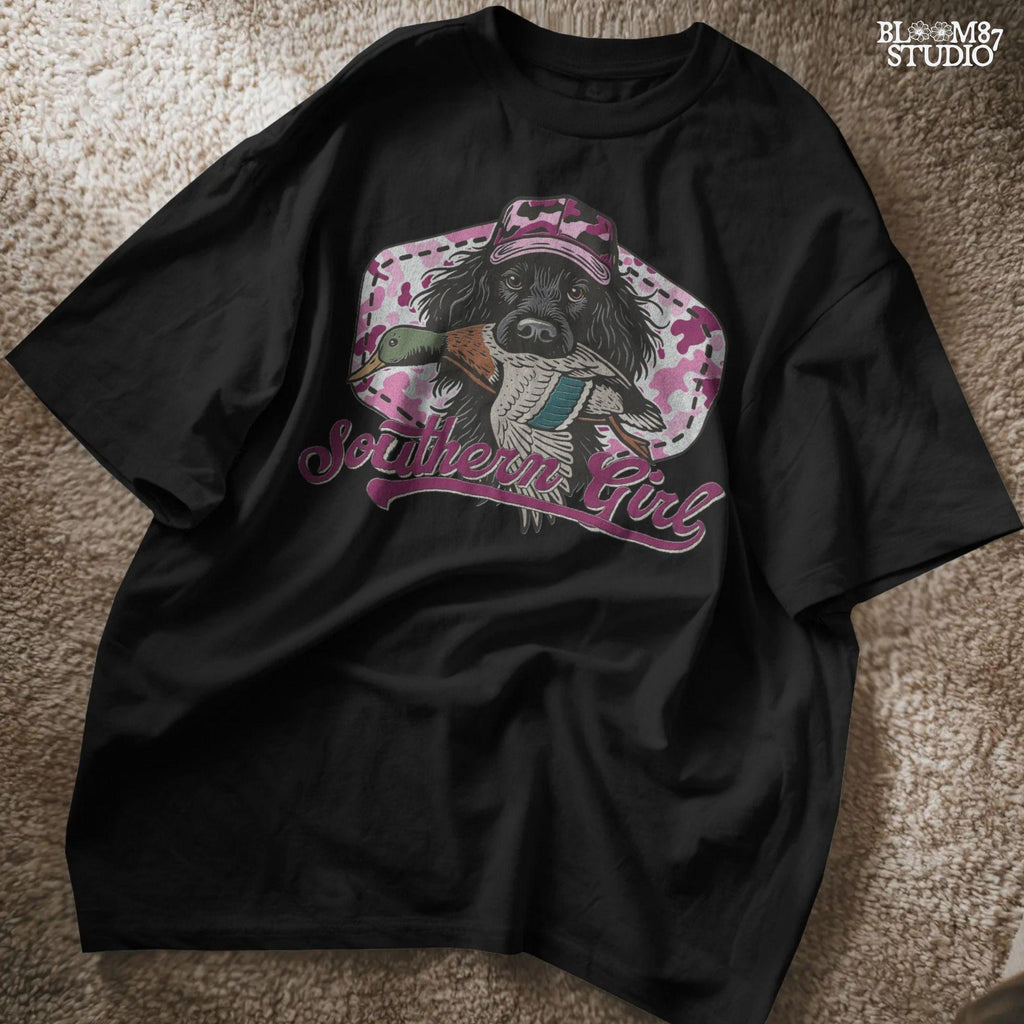 Illustration of a black hunting dog wearing a pink camo hat and holding a mallard duck, with “Southern Girl” text and pink camouflage background.
