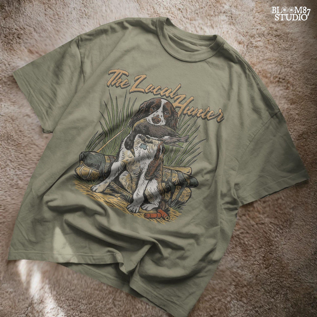 Vintage illustration of a Springer Spaniel hunting dog holding a duck in its mouth with grass, ammo, and hunting gear around, and the phrase “The Local Hunter” above.