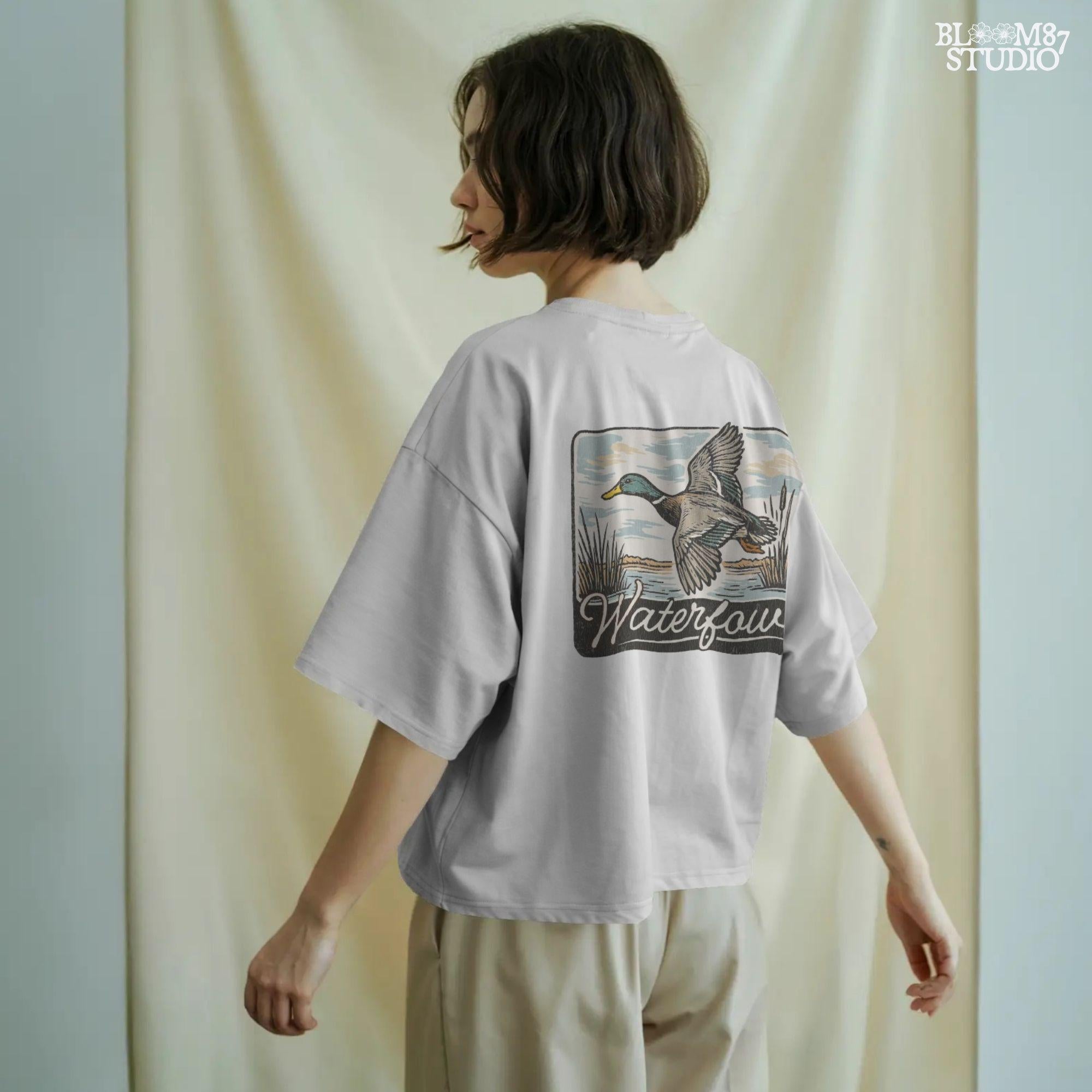 Vintage-style illustration of a flying mallard duck over a marsh with the word “Waterfowl” in script, perfect for duck hunting and outdoor-themed designs.