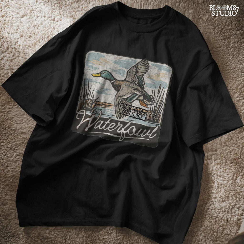 Vintage-style illustration of a flying mallard duck over a marsh with the word “Waterfowl” in script, perfect for duck hunting and outdoor-themed designs.