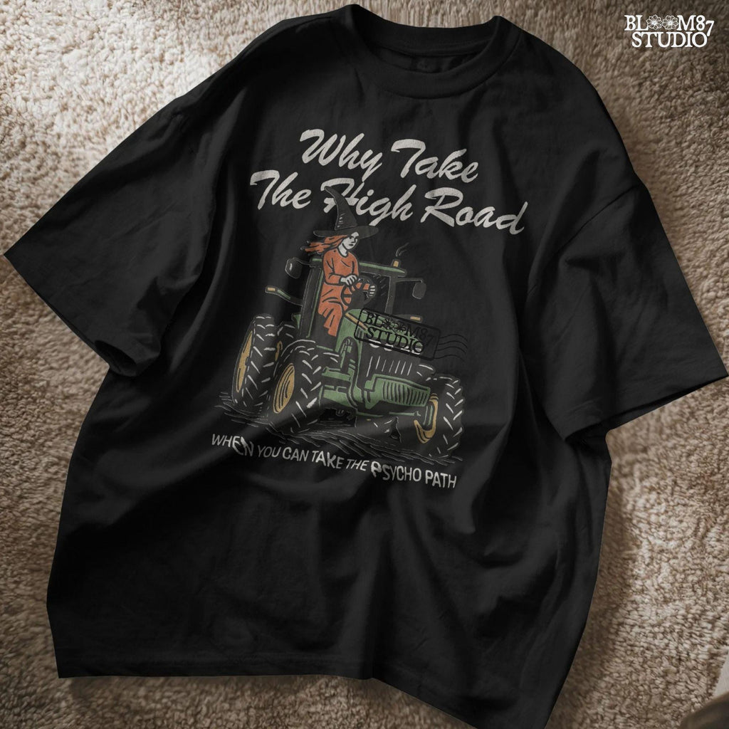 Funny illustration of a red-haired witch in a black hat driving a green tractor with the quote “Why take the high road when you can take the psycho path,” in rustic cartoon style.