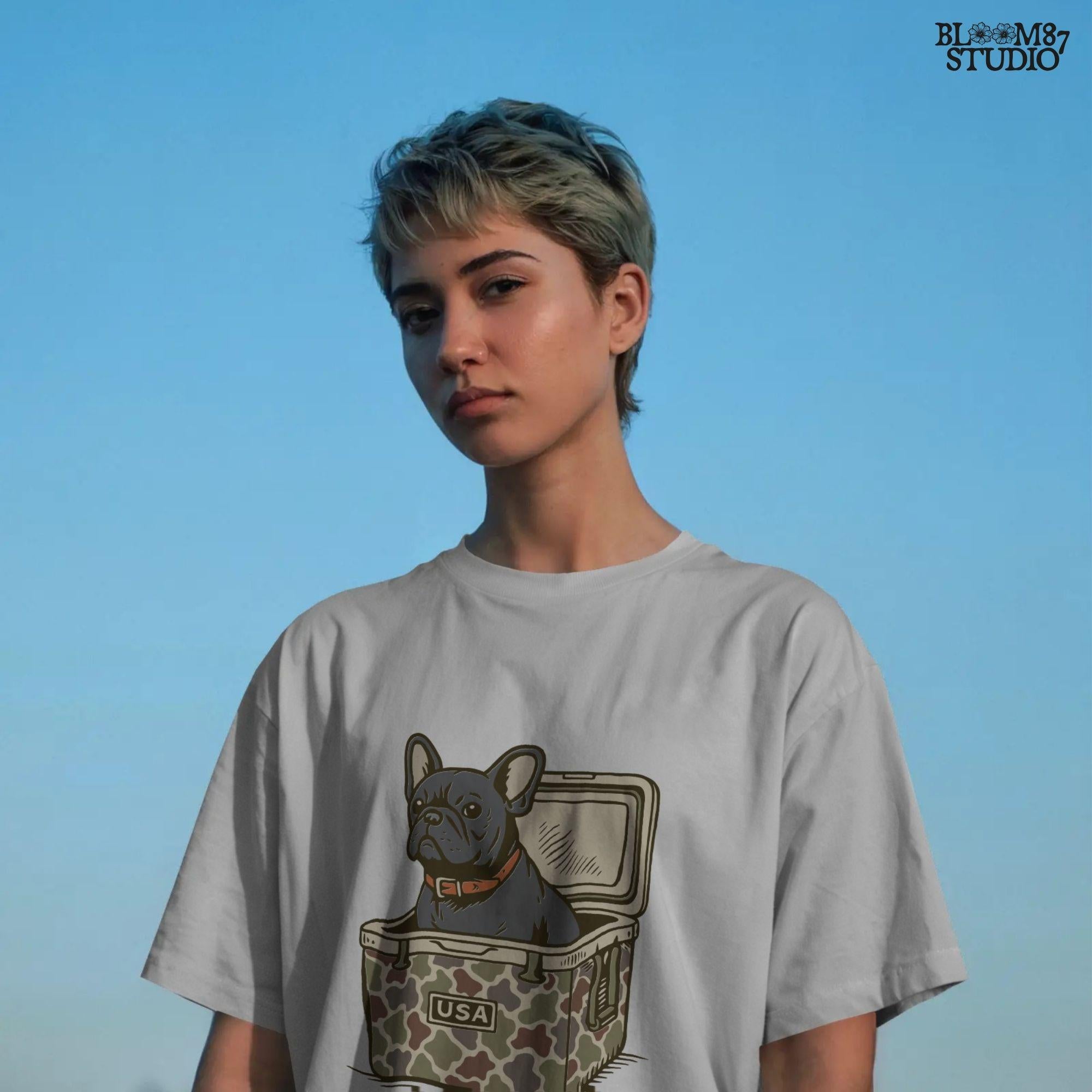 French Bulldog sitting inside a camouflage USA cooler, wearing a red collar, in rustic outdoor style — perfect for patriotic dog lovers and sublimation use.