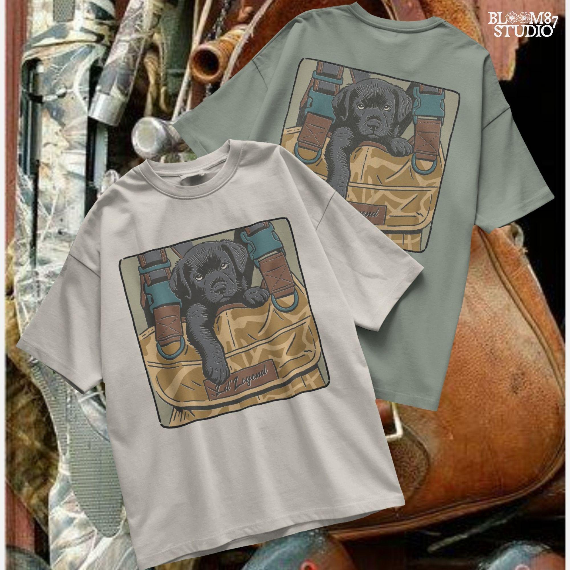 Illustration of a black Labrador puppy resting in a camouflage hunting bag with a “Lil’ Legend” tag – ideal for outdoor-themed sublimation projects.