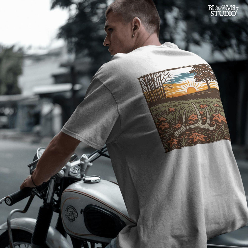 A rustic illustration of a whitetail antler lying in a fall field with orange leaves and a vibrant sunset sky in the background, PNG format for sublimation.