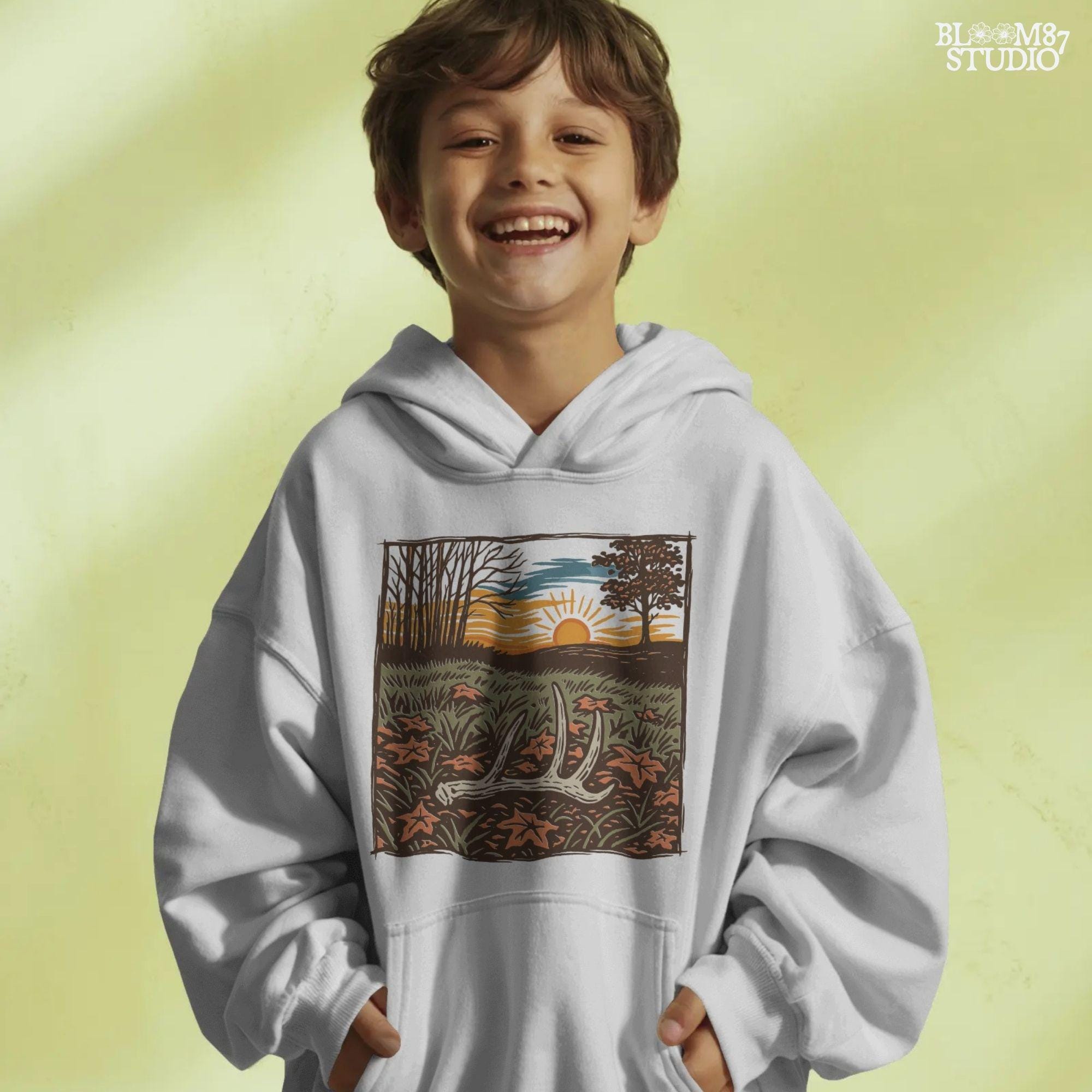 A rustic illustration of a whitetail antler lying in a fall field with orange leaves and a vibrant sunset sky in the background, PNG format for sublimation.