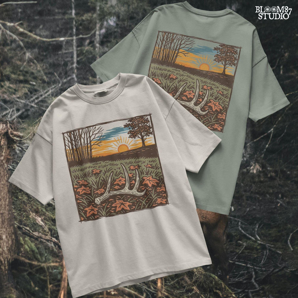 A rustic illustration of a whitetail antler lying in a fall field with orange leaves and a vibrant sunset sky in the background, PNG format for sublimation.