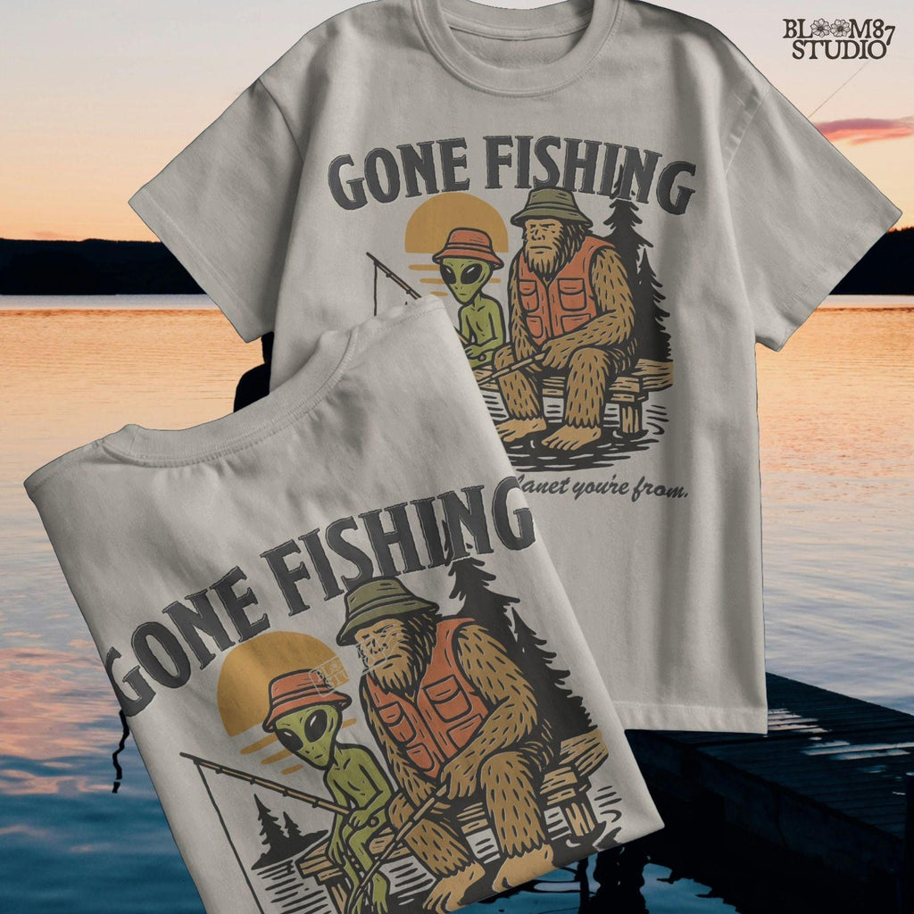 Funny illustration of Bigfoot and an alien fishing together on a lake dock at sunset, wearing fishing hats and vests—perfect for summer and Father’s Day sublimation.