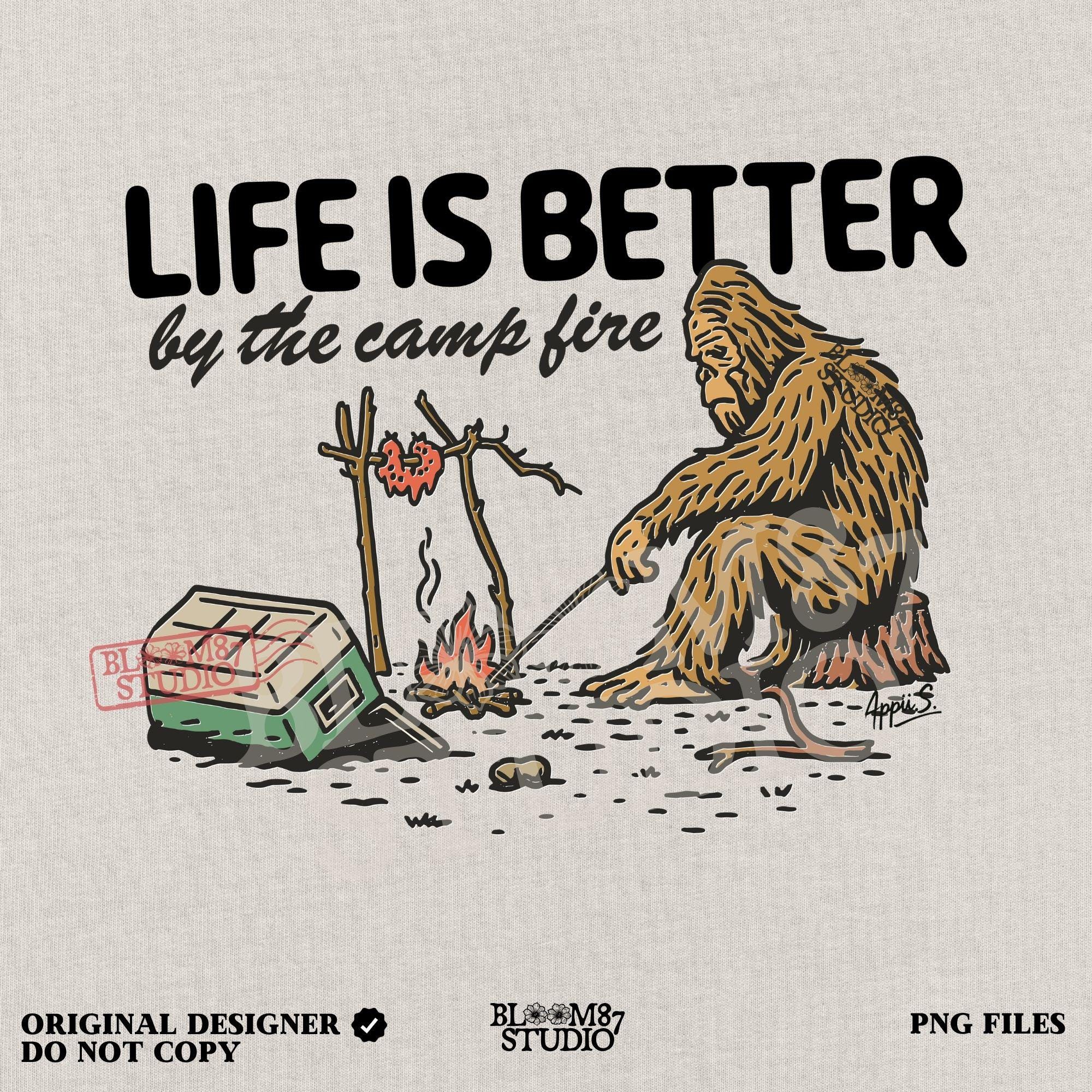 Bigfoot roasting meat over a campfire next to a tipped cooler, with the phrase “Life Is Better by the camp fire” above, illustrated PNG design for outdoor sublimation.