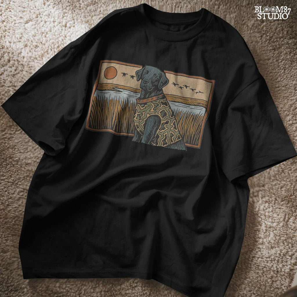 Camo-clad black Labrador retriever sitting in a grassy marsh with flying ducks and a sunset background, digital PNG for hunting dog sublimation designs.