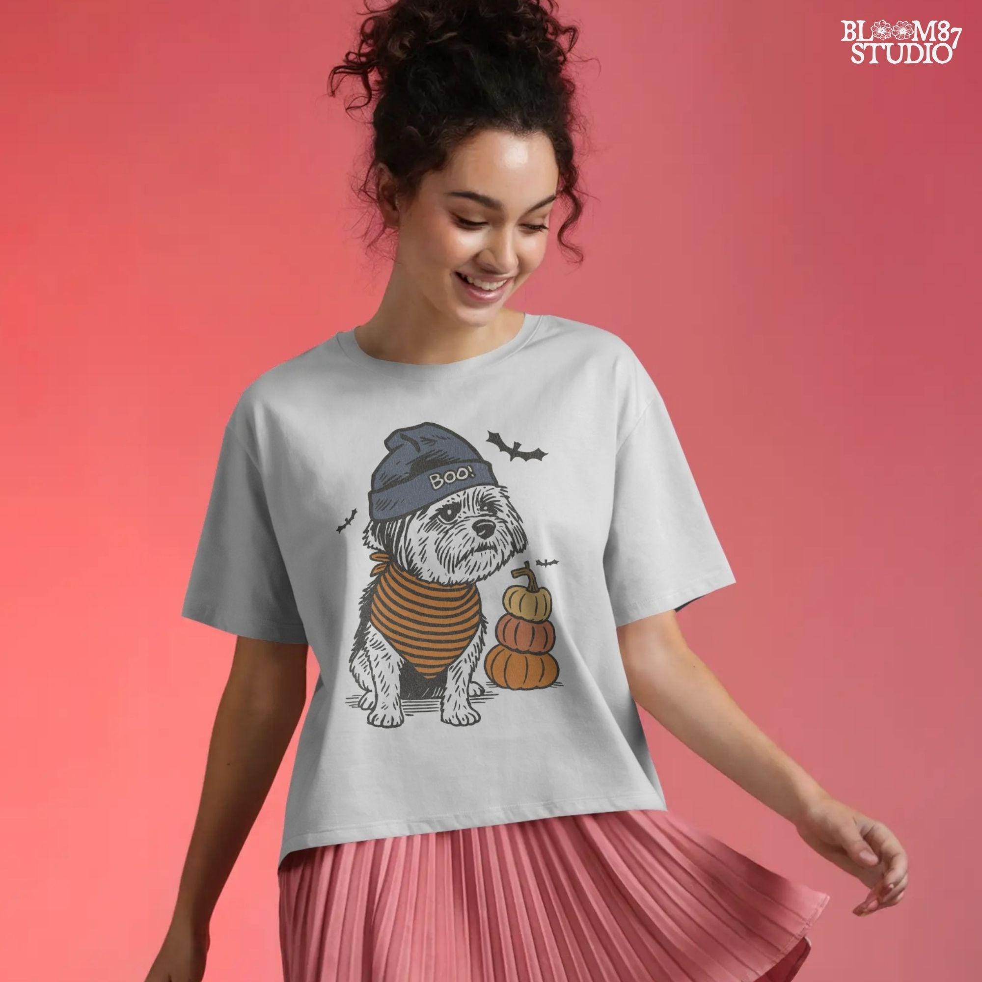 Illustration of a black dog wearing a “BOO!” hat and orange striped bandana, sitting next to stacked pumpkins on a Halloween background.