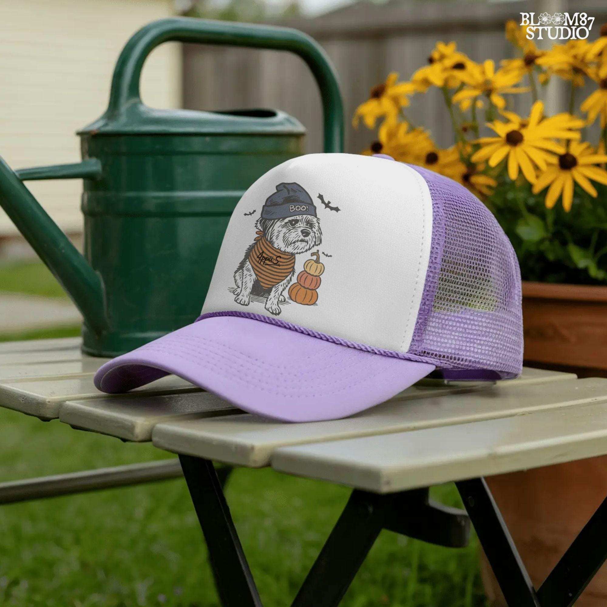 Illustration of a black dog wearing a “BOO!” hat and orange striped bandana, sitting next to stacked pumpkins on a Halloween background.