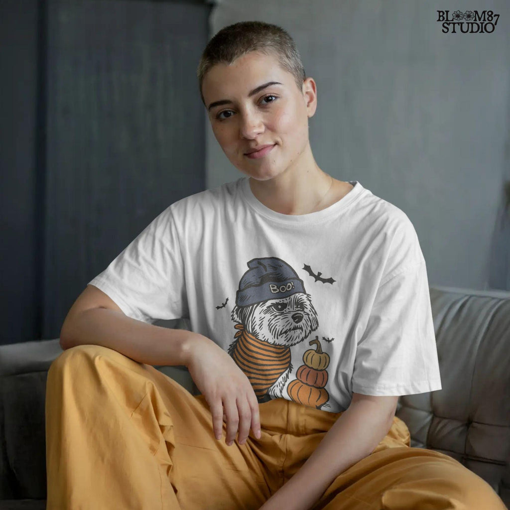 Illustration of a black dog wearing a “BOO!” hat and orange striped bandana, sitting next to stacked pumpkins on a Halloween background.