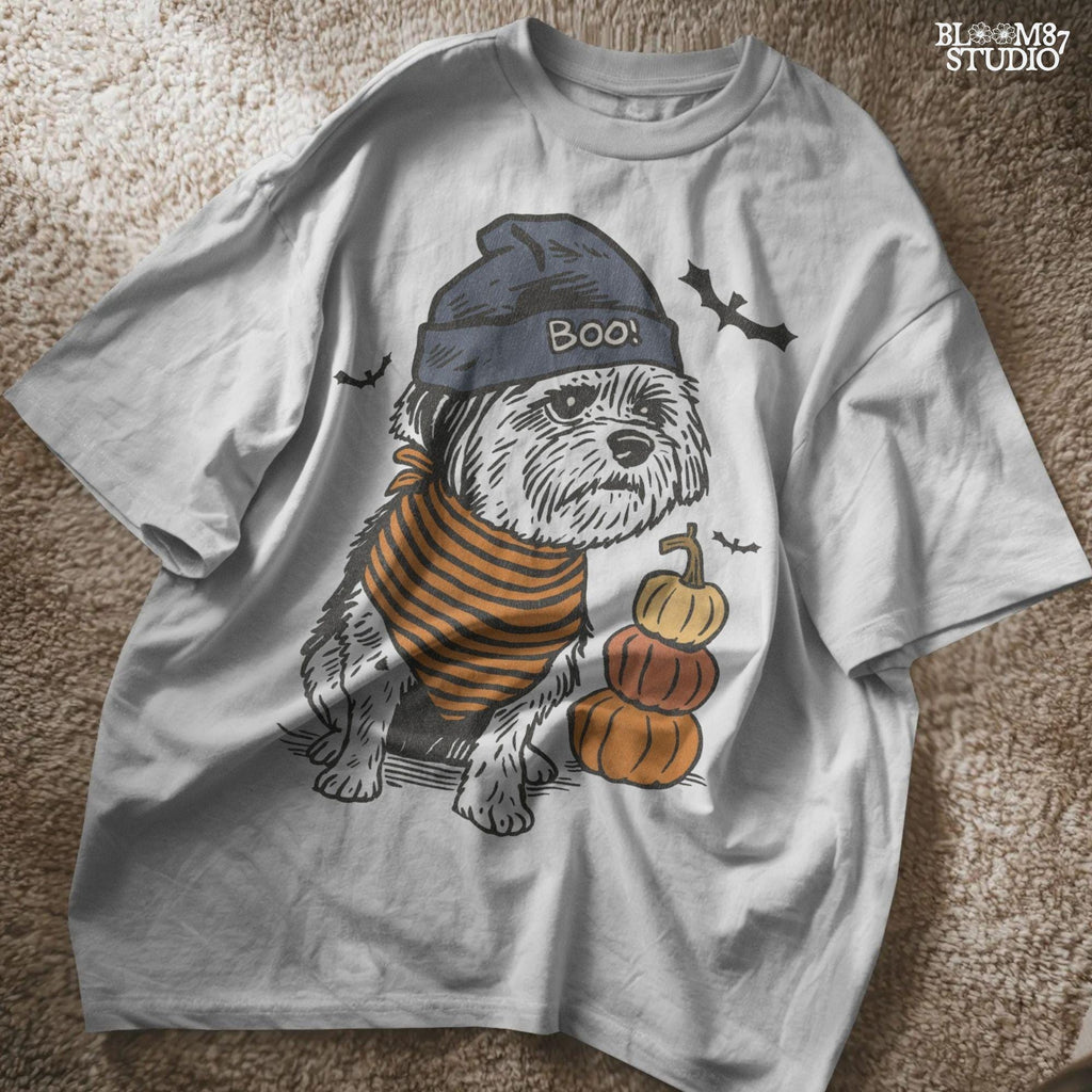 Illustration of a black dog wearing a “BOO!” hat and orange striped bandana, sitting next to stacked pumpkins on a Halloween background.