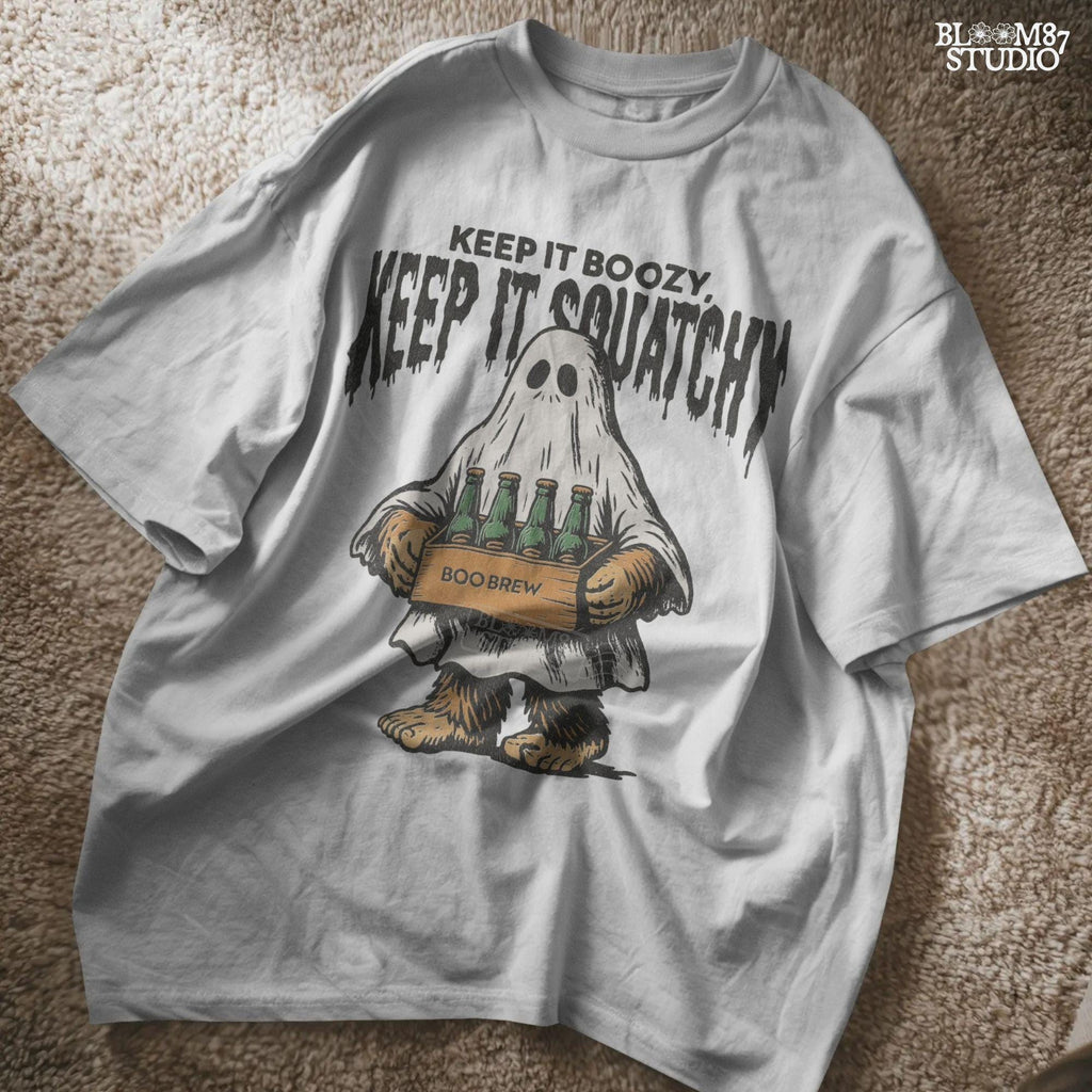 Funny Bigfoot dressed as a ghost holding a six-pack labeled “Boo Brew,” with spooky text “Keep It Boozy, Keep It Squatchy” above.