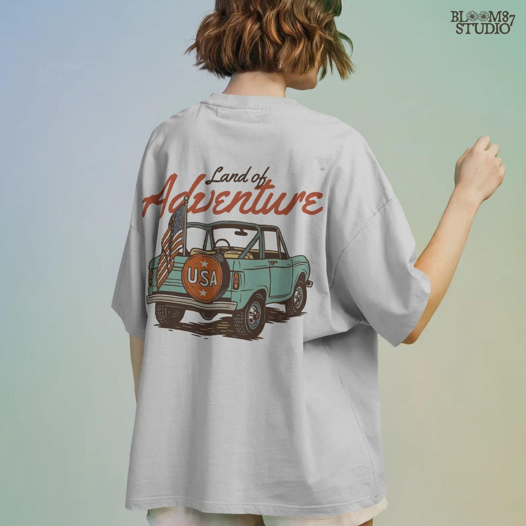 Vintage convertible truck with “USA” spare tire and American flag, text reads “Land of Adventure,” in a retro patriotic illustration style.