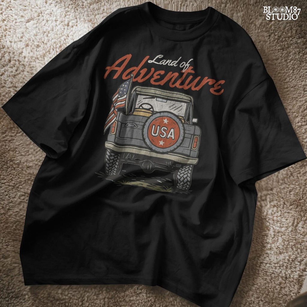 Vintage offroad truck seen from the back with “USA” spare tire and waving American flag, text reads “Land of Adventure” in retro patriotic style.