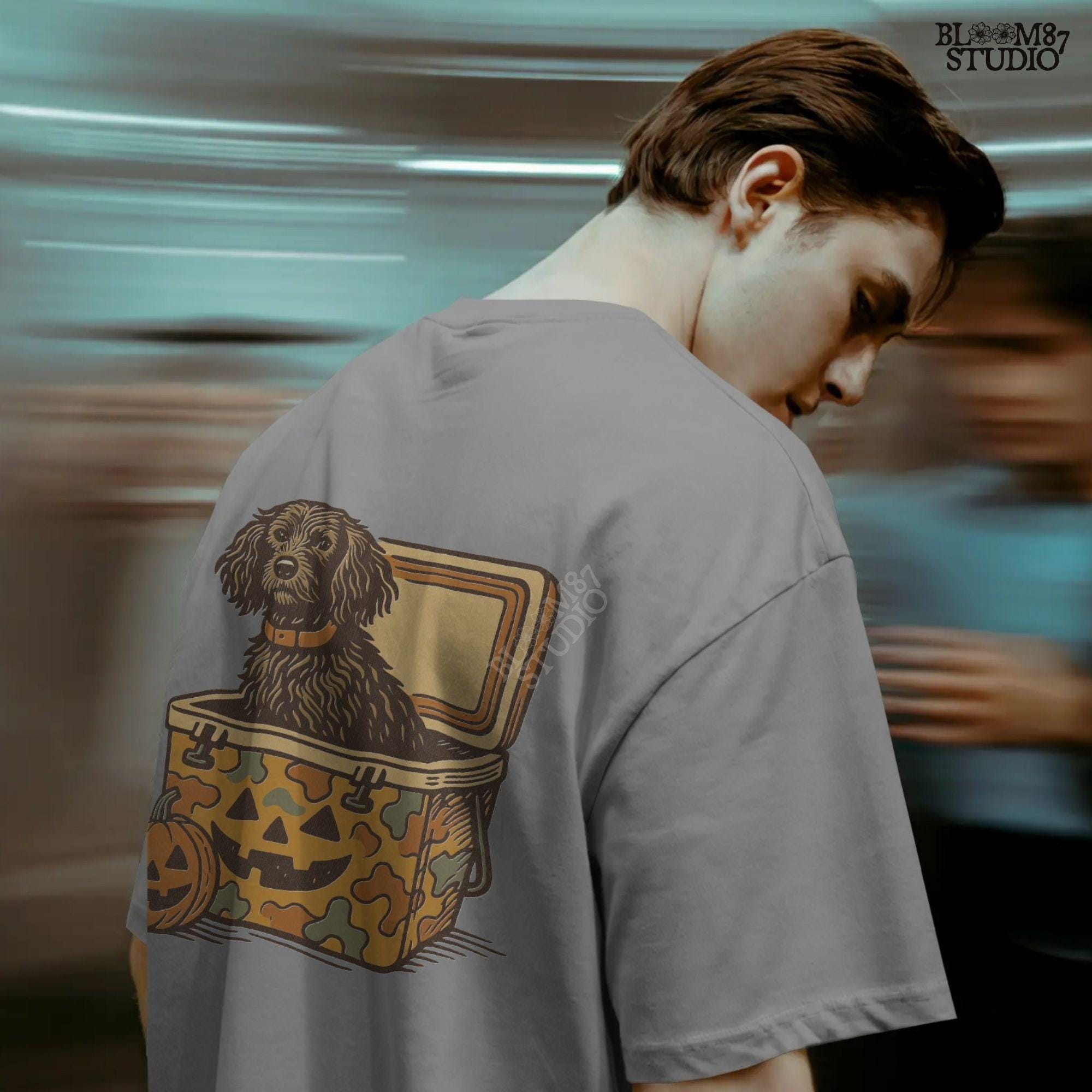 Halloween-themed PNG of a fluffy dog sitting inside a pumpkin-faced camouflage cooler, with jack-o’-lantern pumpkins next to it.