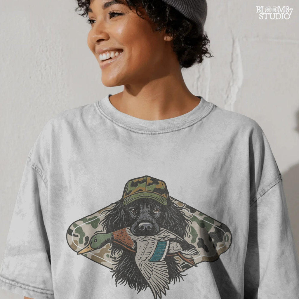 Illustration of a long-haired duck hunting dog wearing a camouflage hat, holding a mallard duck in its mouth, with a camo background design.