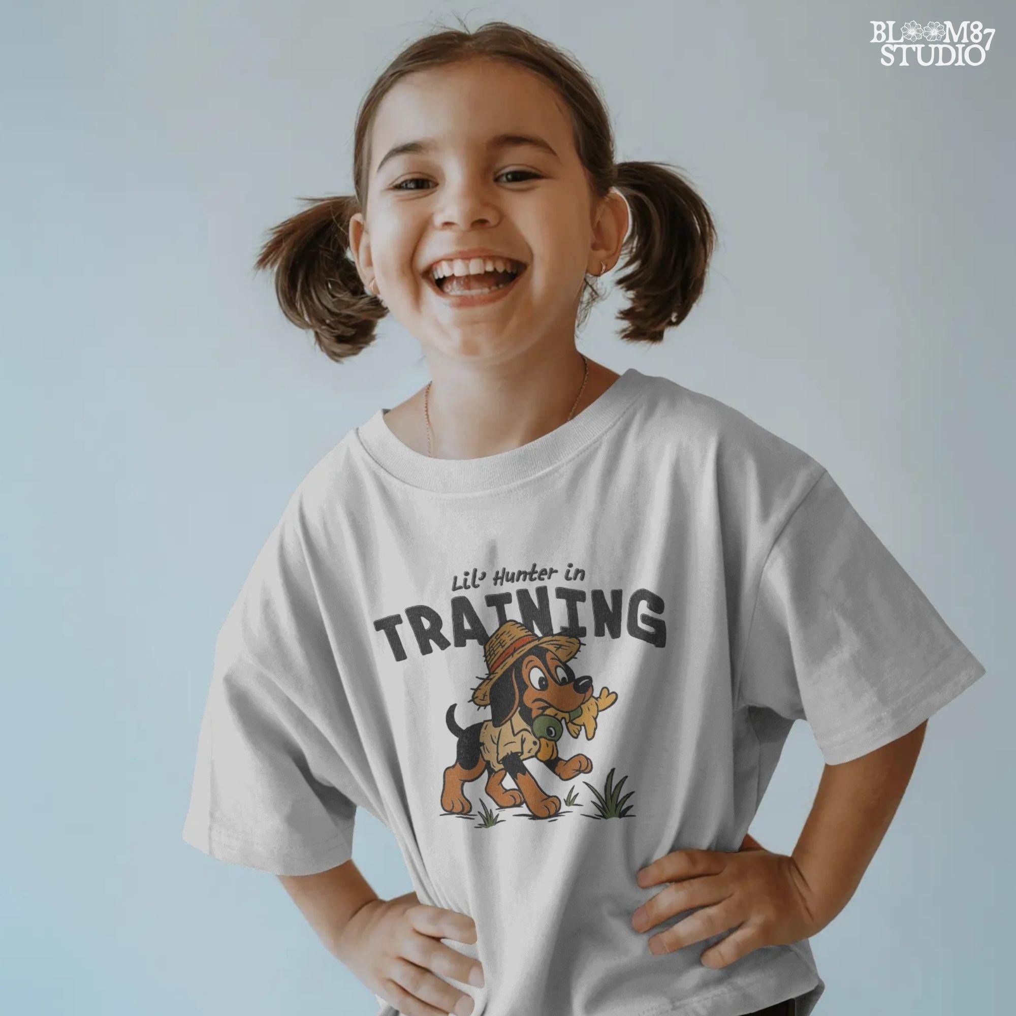 Cartoon hunting dog wearing straw hat and camo shirt holding duck toy in mouth with “Lil’ Hunter in Training” text – cute PNG for kids sublimation.