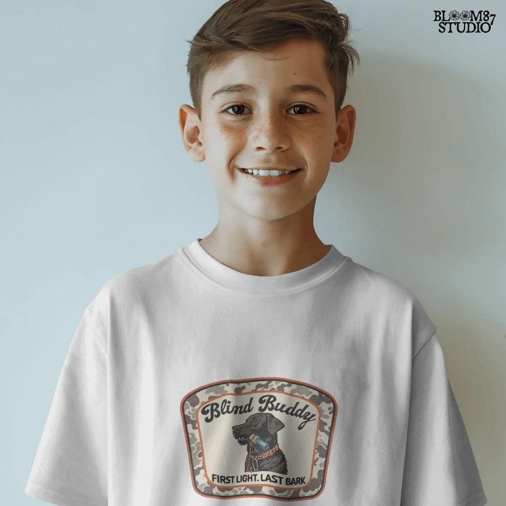 Black labrador dog holding a duck call in its mouth, centered in a camouflage hunting patch with text “Blind Buddy – First Light. Last Bark”