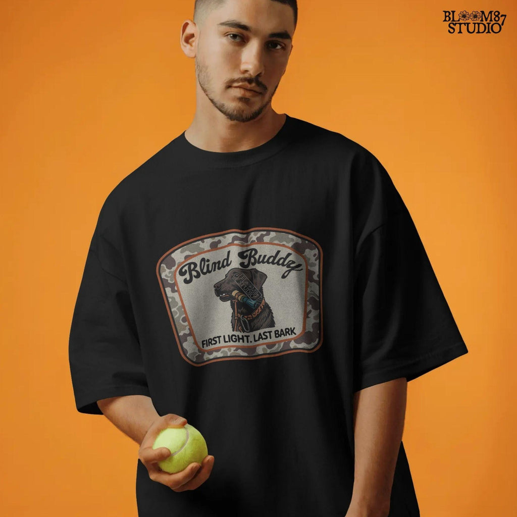 Black labrador dog holding a duck call in its mouth, centered in a camouflage hunting patch with text “Blind Buddy – First Light. Last Bark”