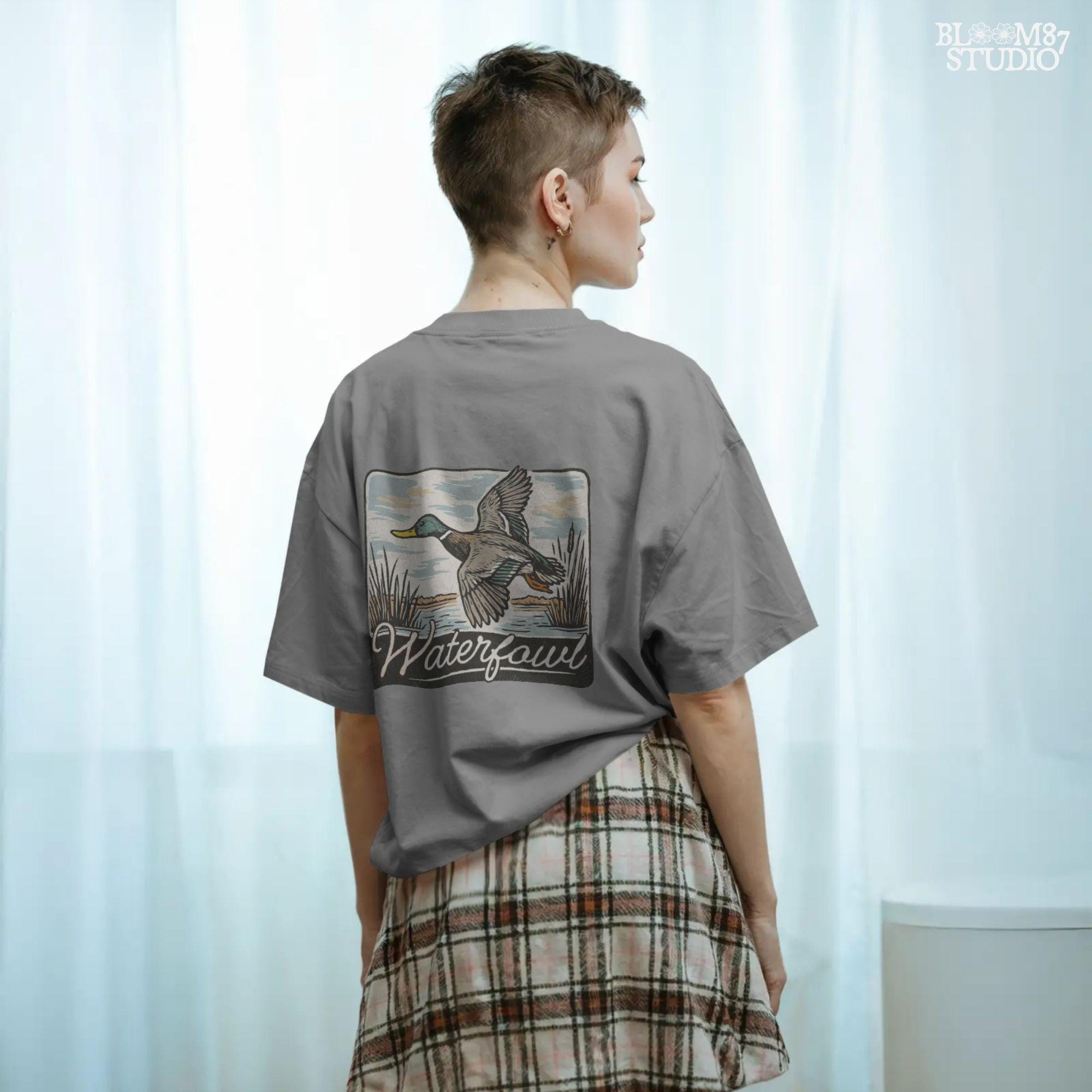 Vintage-style illustration of a flying mallard duck over a marsh with the word “Waterfowl” in script, perfect for duck hunting and outdoor-themed designs.