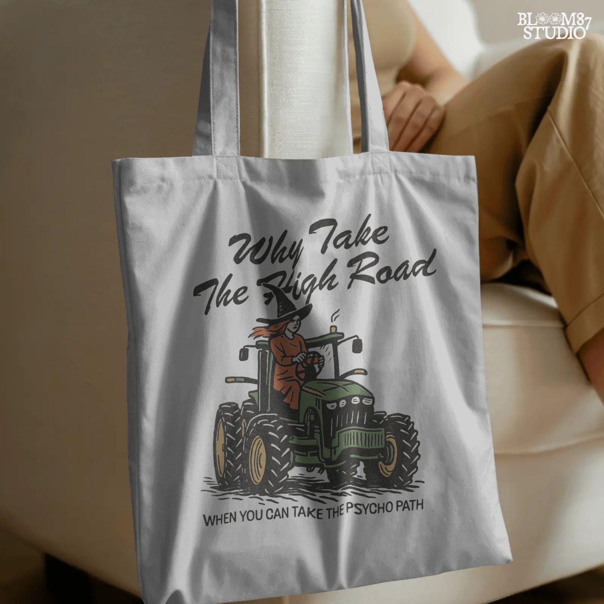 Funny illustration of a red-haired witch in a black hat driving a green tractor with the quote “Why take the high road when you can take the psycho path,” in rustic cartoon style.