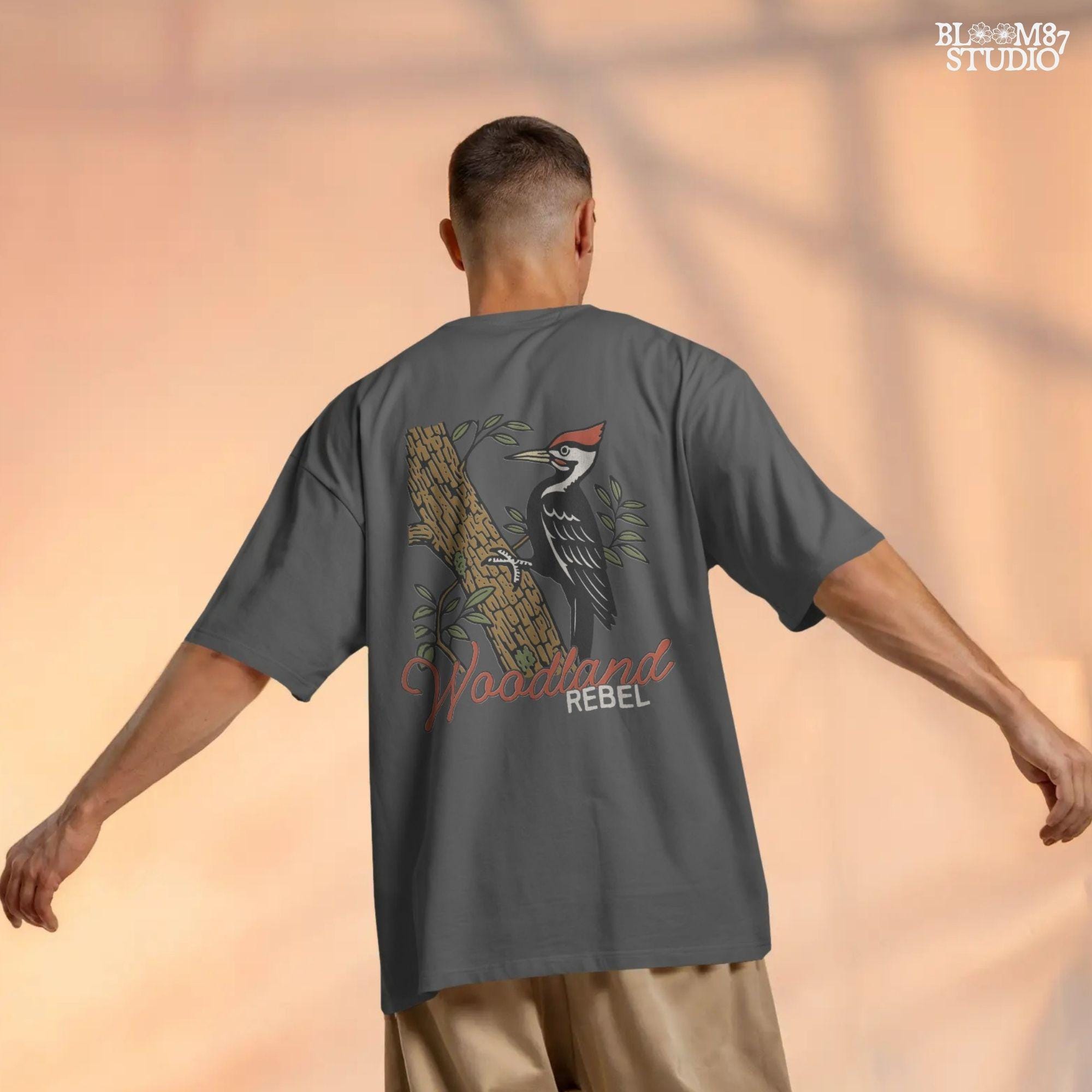 Vintage woodpecker perched on a tree trunk with green leaves and the word “Woodland” in rustic script, fall-themed forest sublimation PNG.