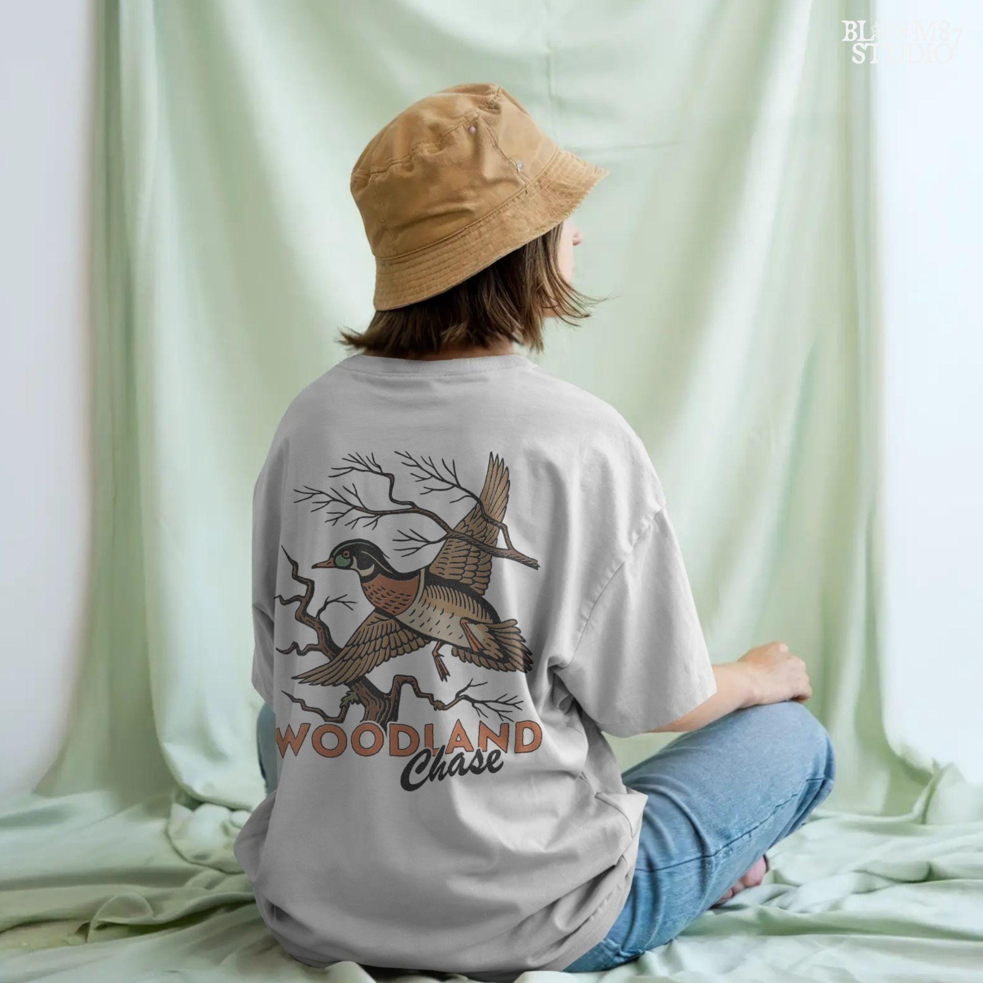 Vintage wood duck flying over bare branches with “Woodland Chase” text in rustic orange and black; sublimation PNG for hunting or fall apparel.