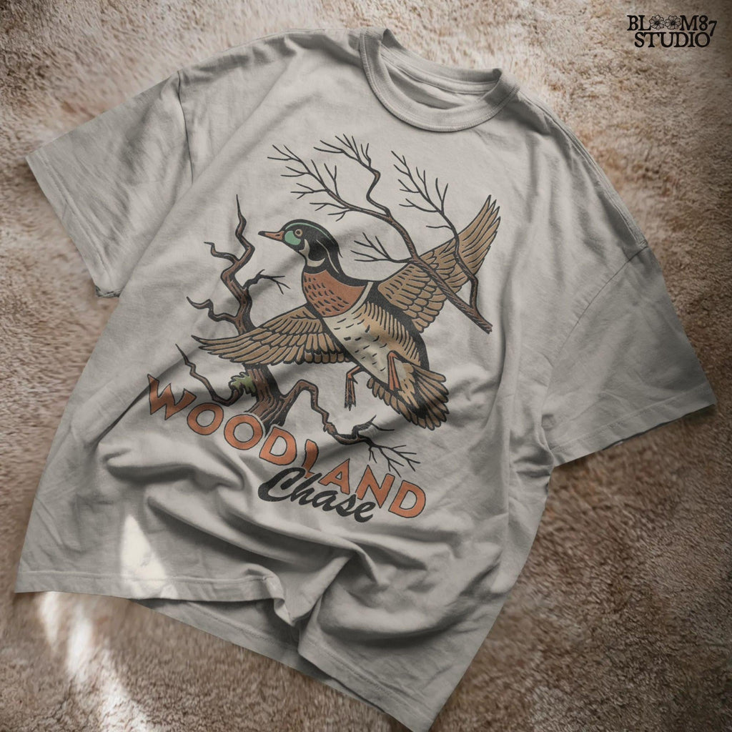 Vintage wood duck flying over bare branches with “Woodland Chase” text in rustic orange and black; sublimation PNG for hunting or fall apparel.