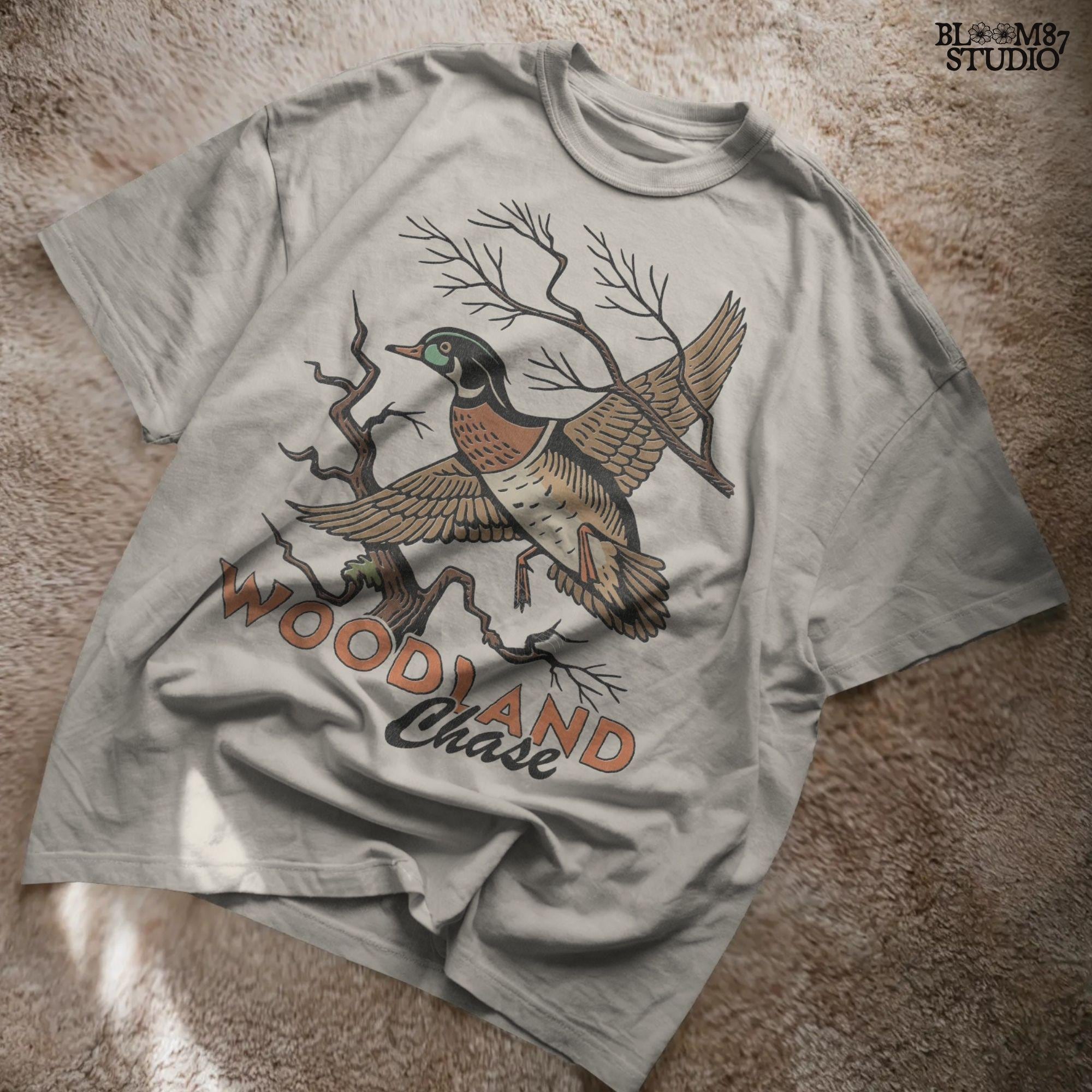 Vintage wood duck flying over bare branches with “Woodland Chase” text in rustic orange and black; sublimation PNG for hunting or fall apparel.