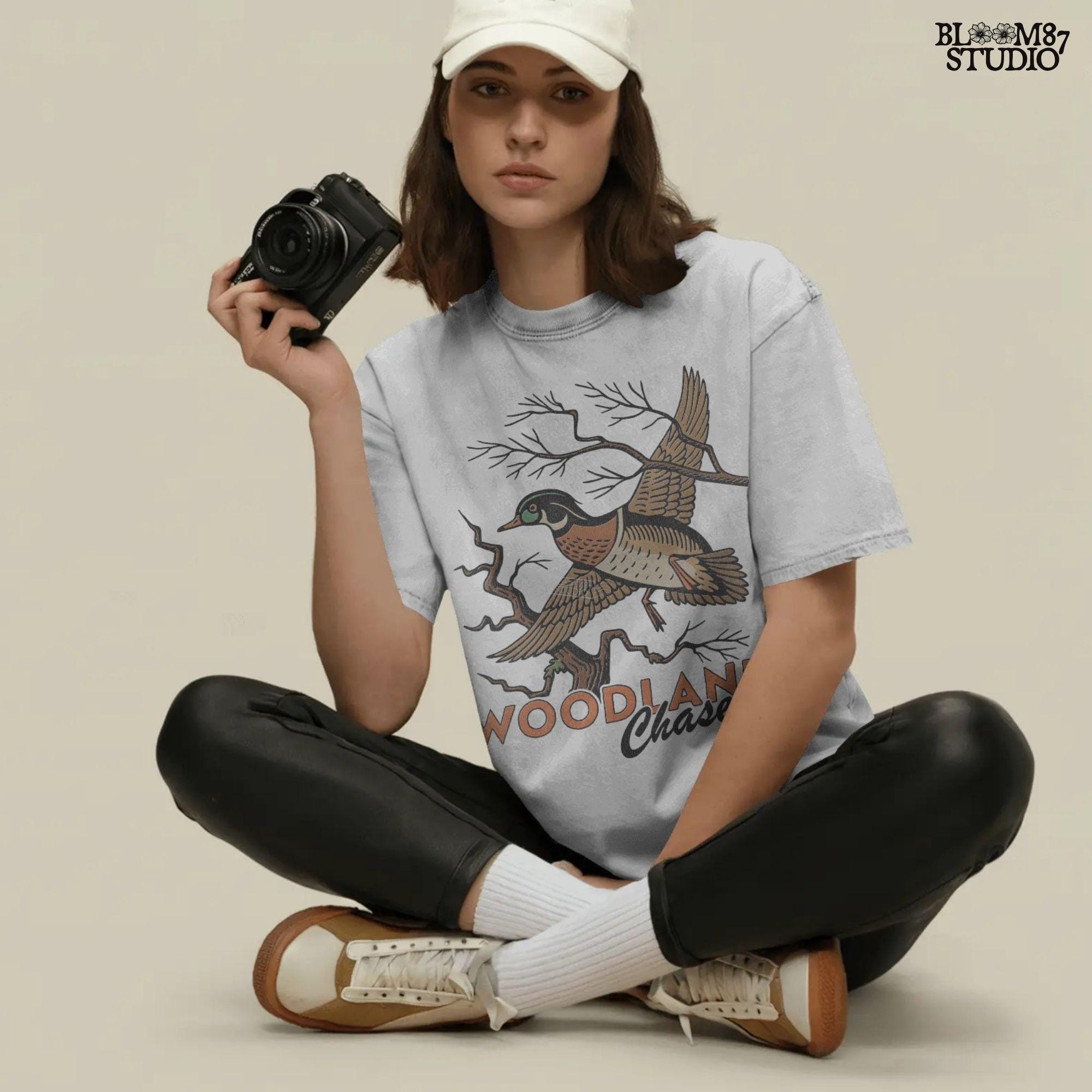 Vintage wood duck flying over bare branches with “Woodland Chase” text in rustic orange and black; sublimation PNG for hunting or fall apparel.