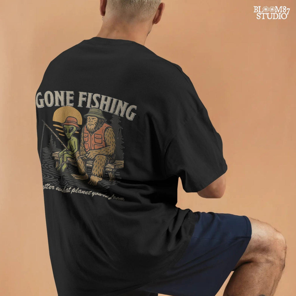 Funny illustration of Bigfoot and an alien fishing together on a lake dock at sunset, wearing fishing hats and vests—perfect for summer and Father’s Day sublimation.