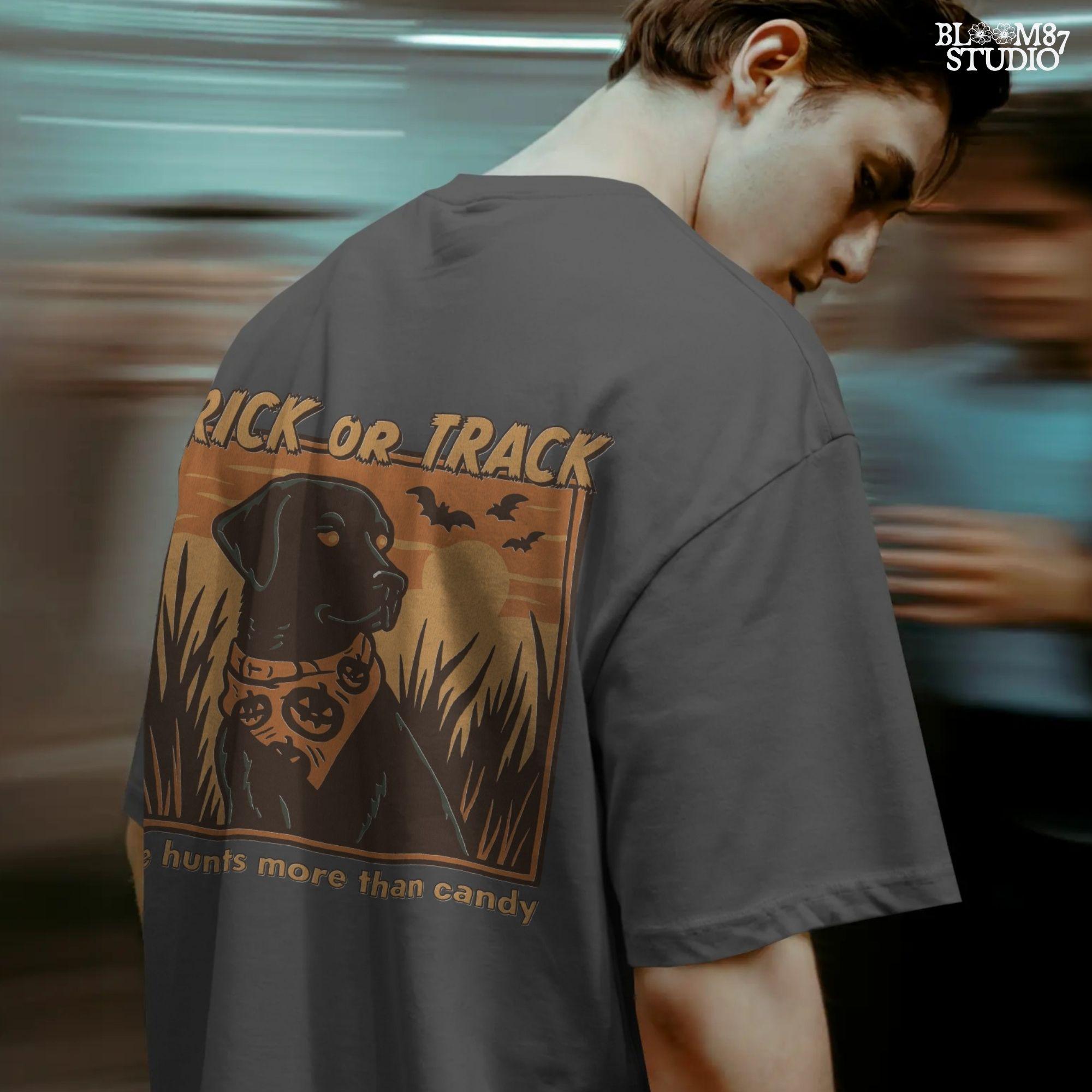 Halloween PNG of a black lab hunting dog wearing a pumpkin bandana with bats, sunset, and text “Trick or Track – He Hunts More Than Candy”