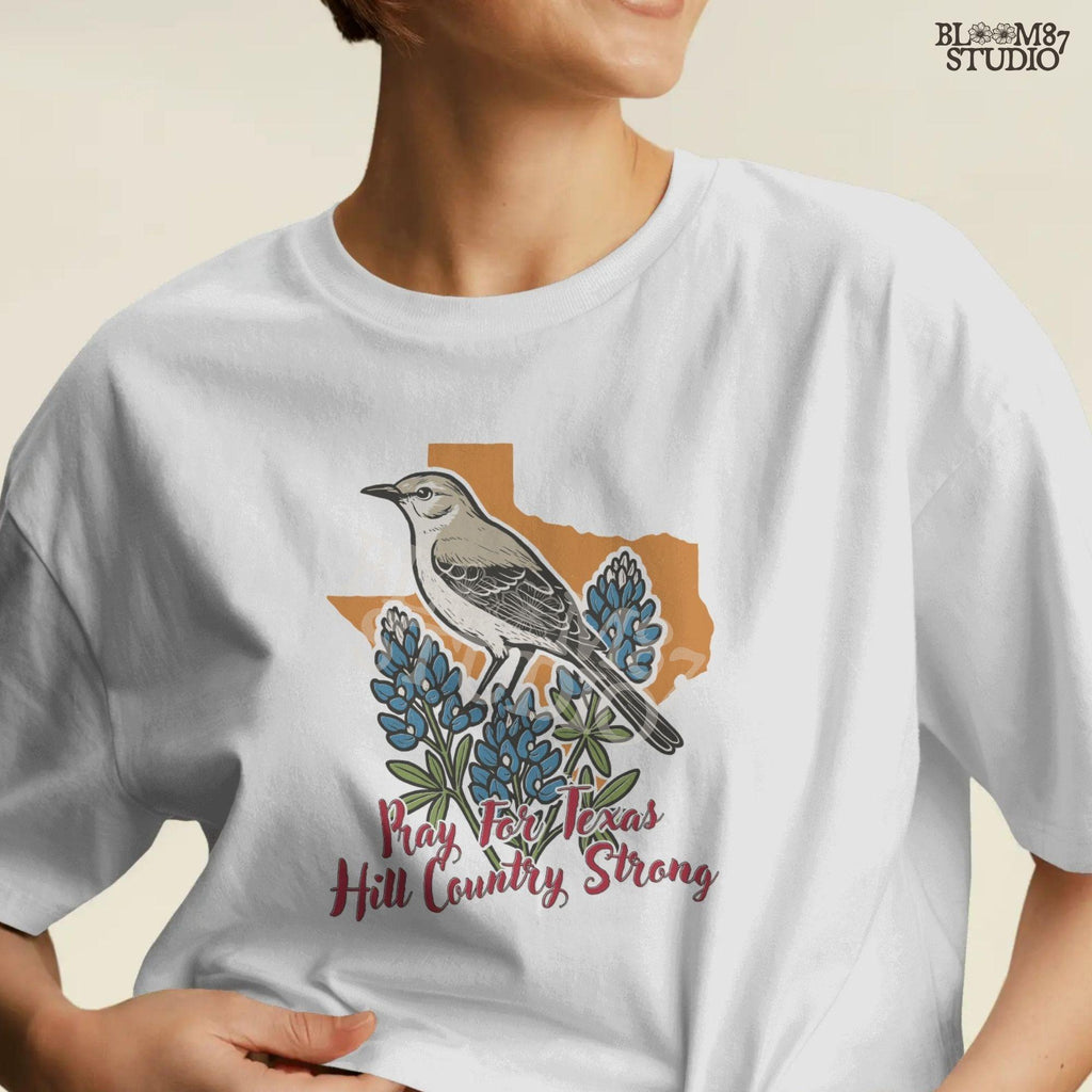 Illustration of a mockingbird on bluebonnets in front of Texas state outline with text “Pray for Texas Hill Country Strong,” designed for sublimation and awareness.