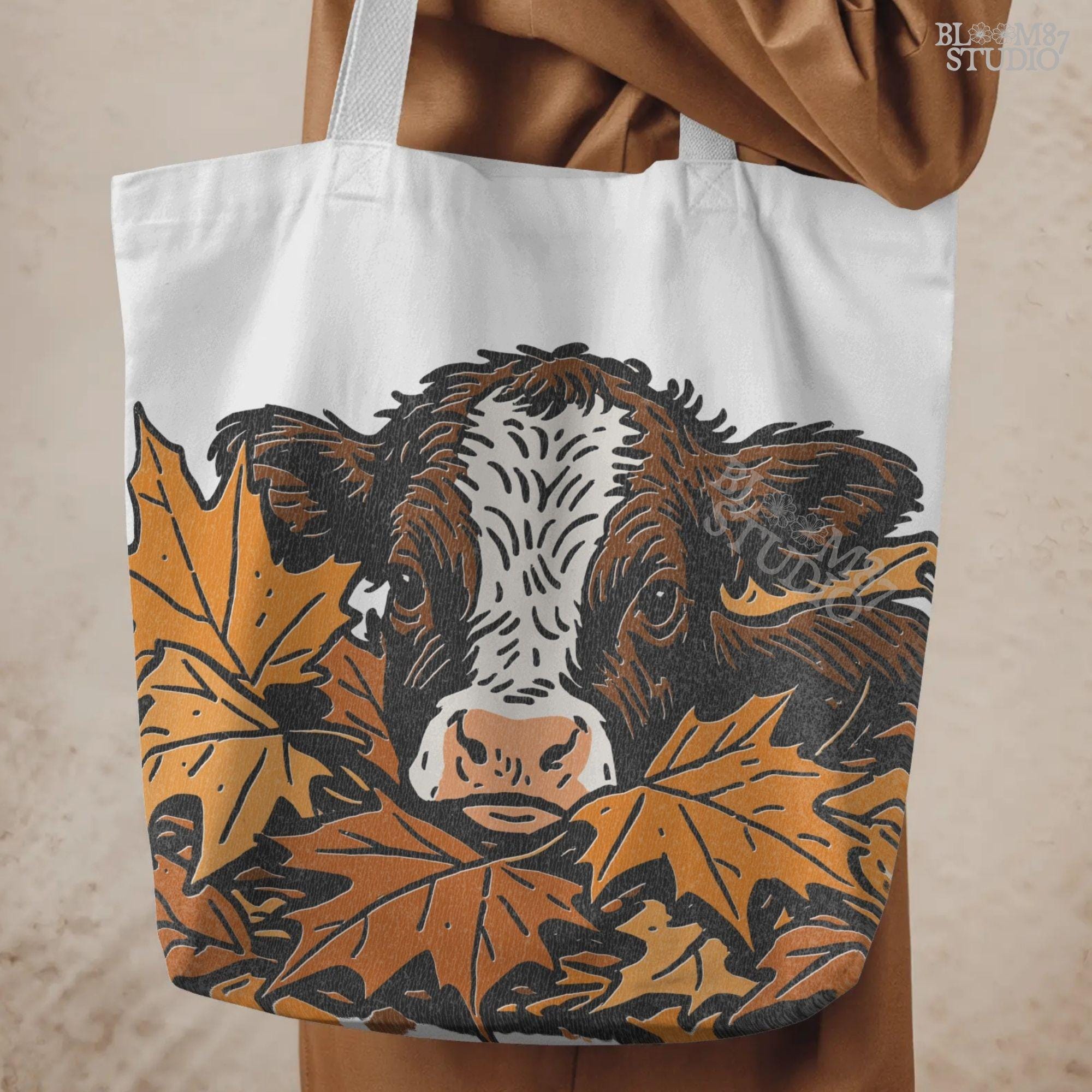 Cute brown and white highland calf resting in a pile of orange and brown fall maple leaves, perfect for autumn sublimation projects